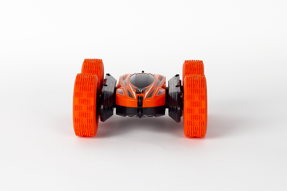 Orange and black remote-controlled stunt car on white surface.