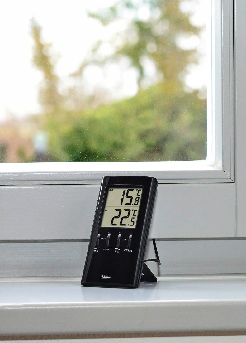 Un termometro nero su un davanzale, che mostra le temperature interne ed esterne.