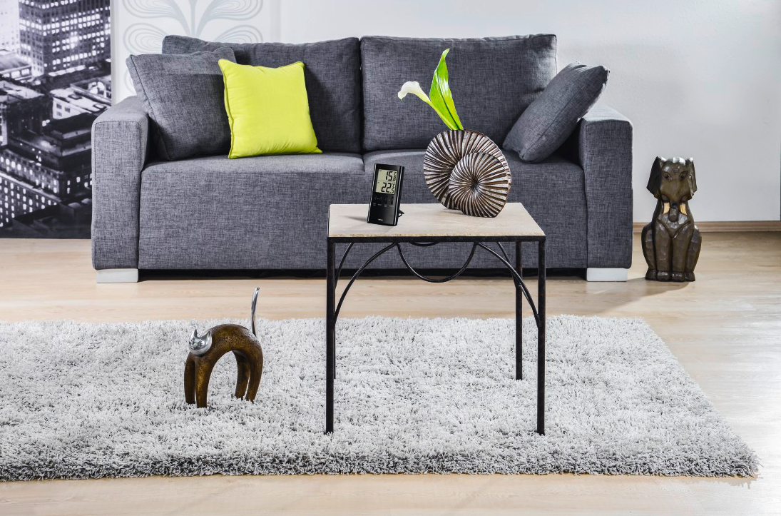 Divano grigio, cuscino verde lime, tavolo bianco con decorazioni, tappeto grigio e scultura di gatto.