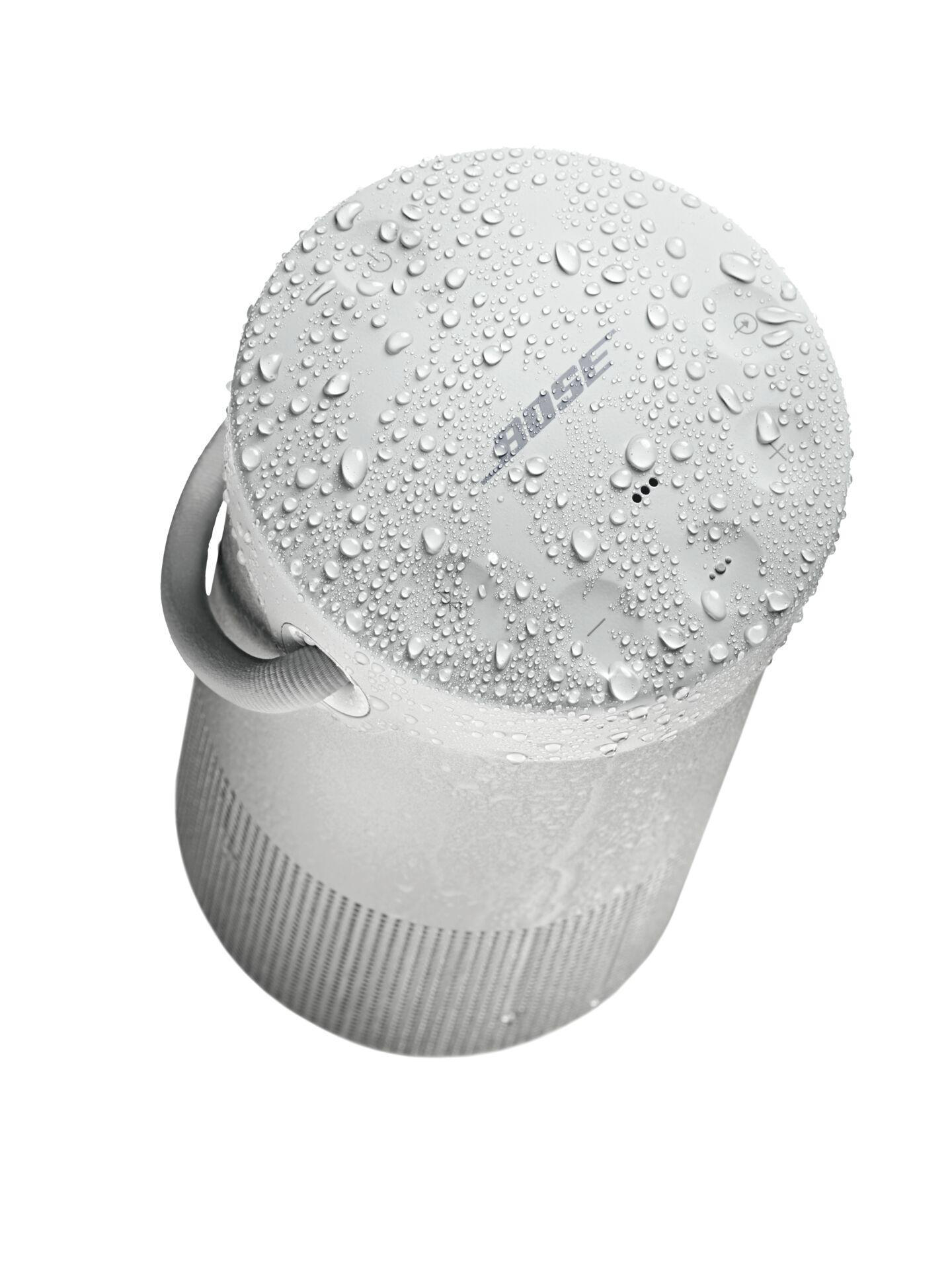 Weißer Bose-Lautsprecher mit Wassertropfen bedeckt. Der Lautsprecher hat einen Griff und ein Gitter.