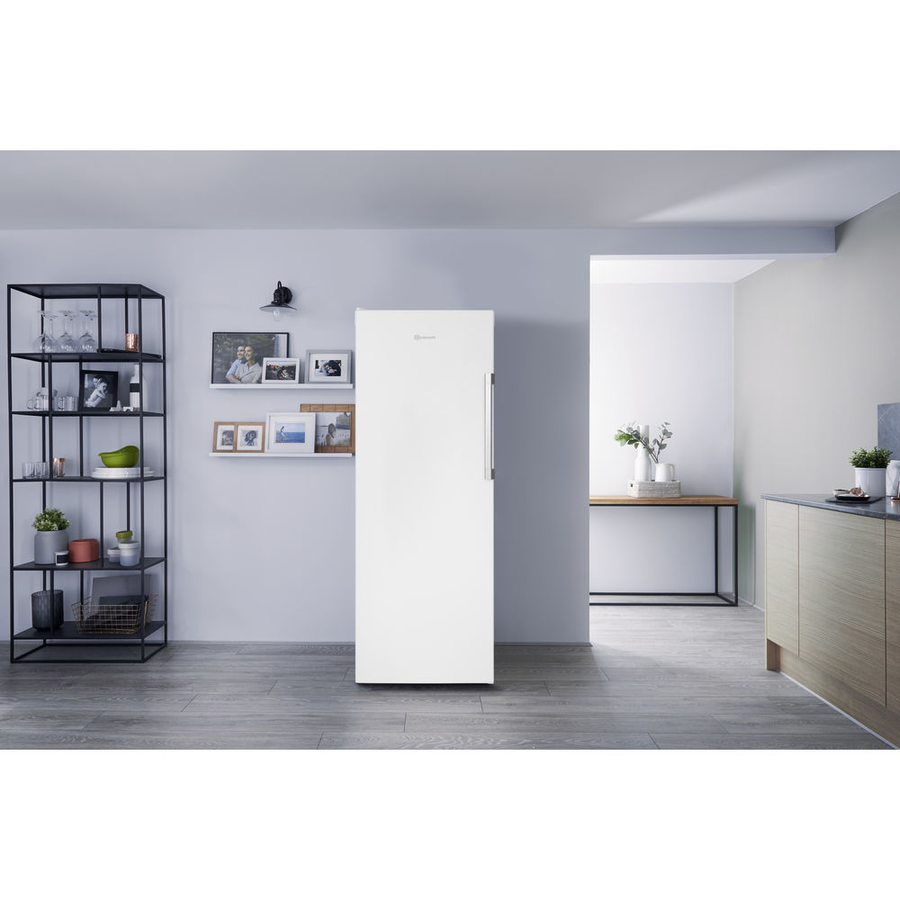 Ein weißer Kühlschrank steht in einem Raum mit Regalen, Bildern und einem Tisch.