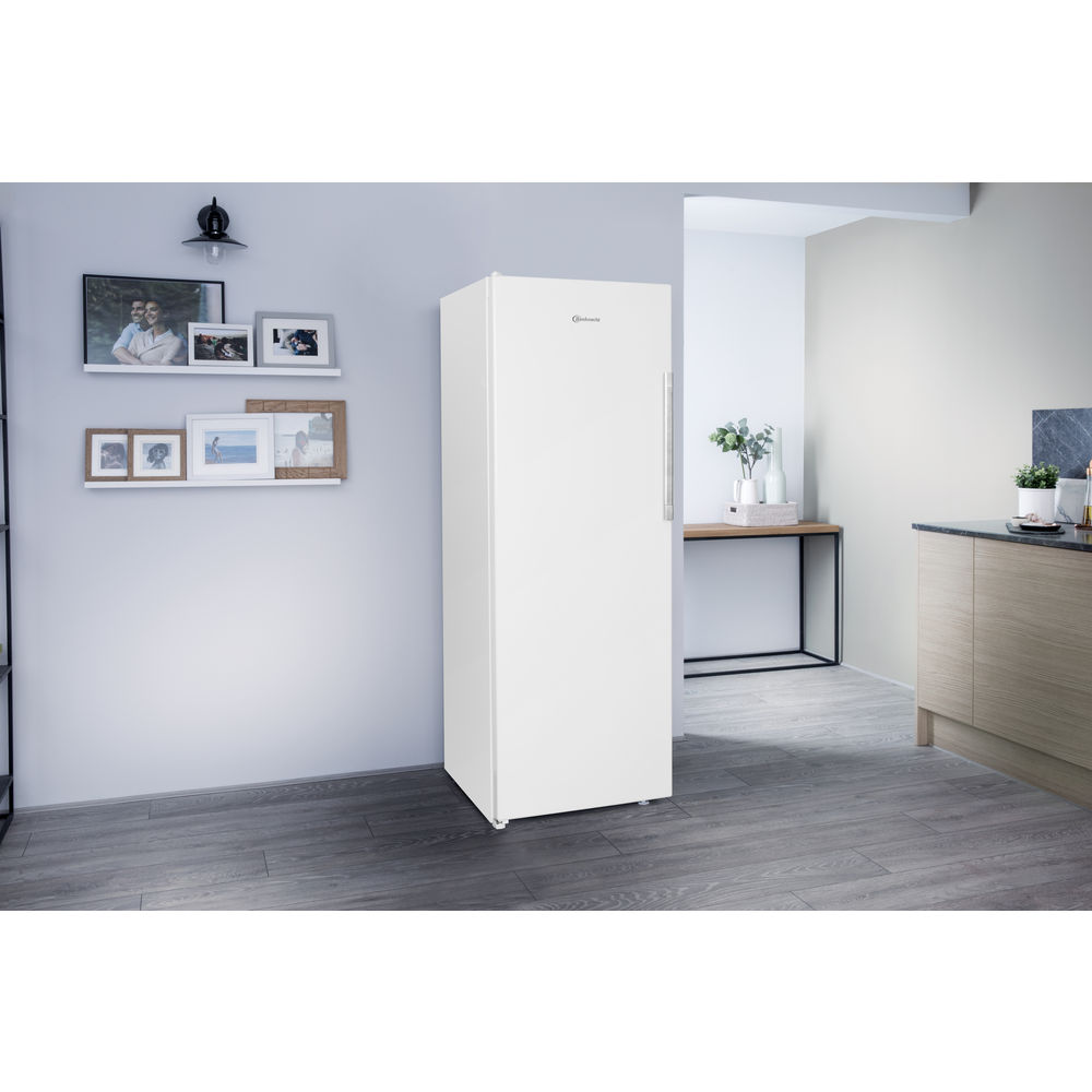 Weißer Kühlschrank steht aufrecht, neben einer Wand mit Bildern und Regalen. Holzfußboden.