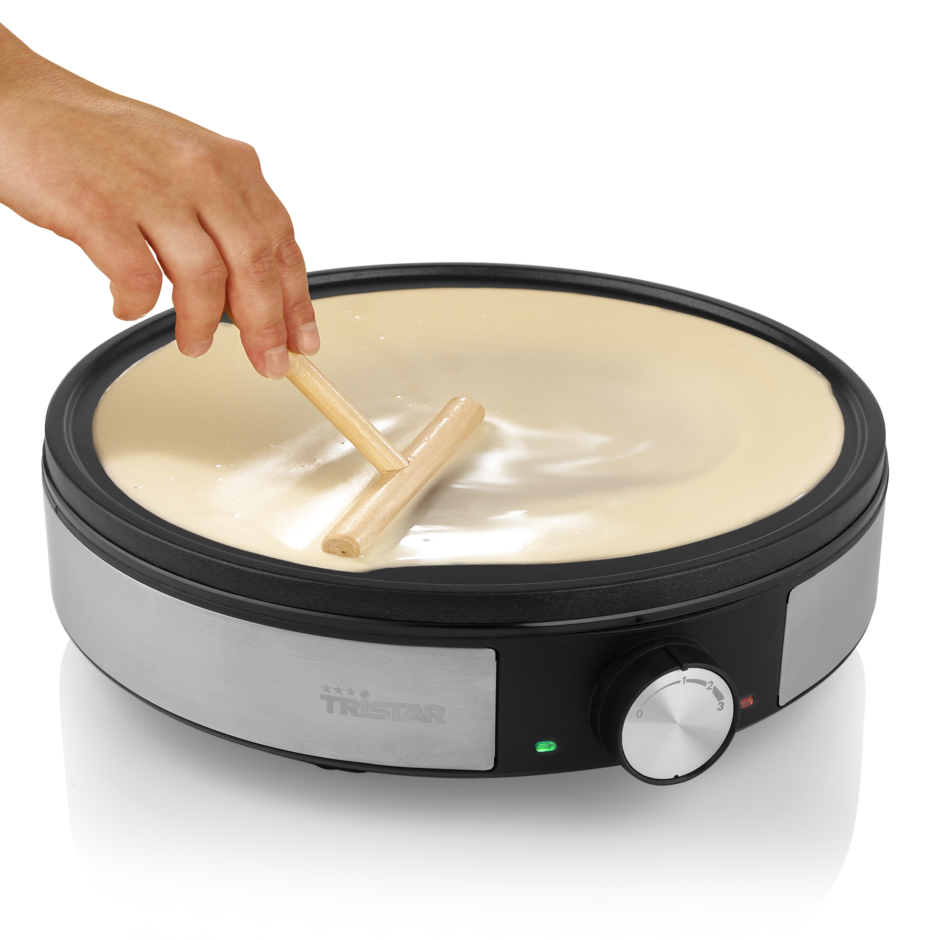 Eine Hand verwendet ein Holzwerkzeug auf einem Crêpe-Maker, der mit Teig gefüllt ist.