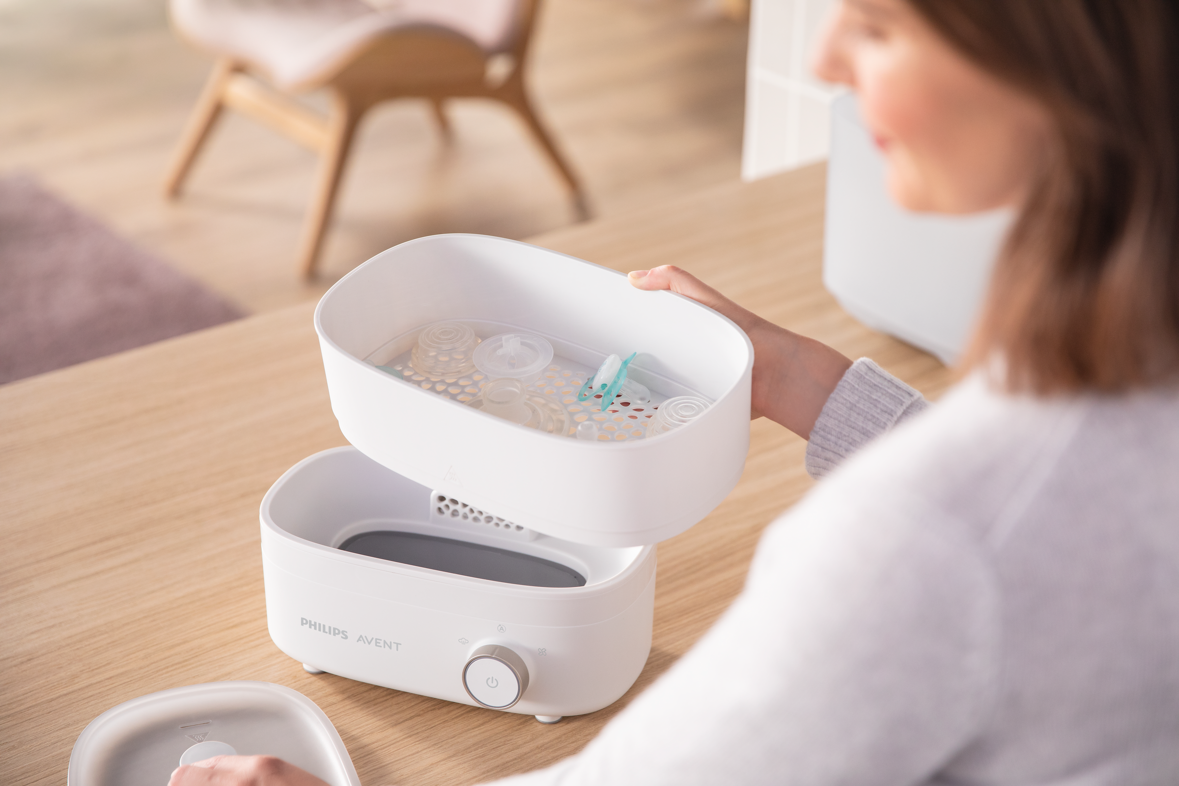Una donna tiene uno sterilizzatore bianco Philips Avent. È aperto, mostrando bottiglie e componenti all'interno.