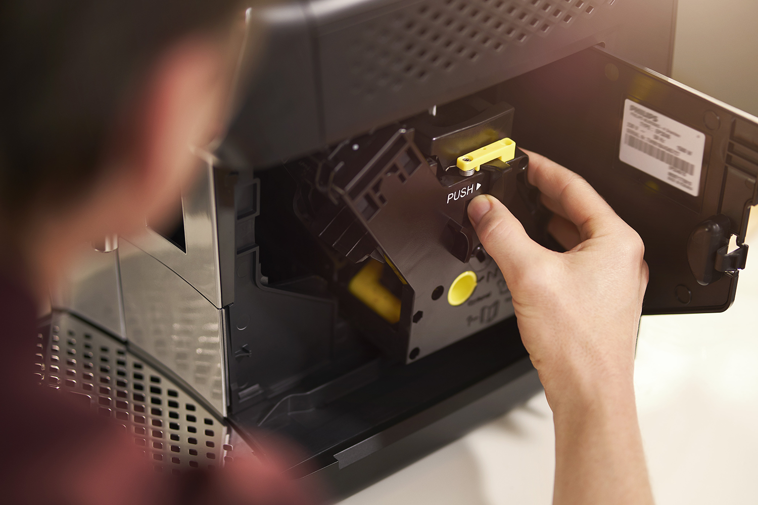 Person replacing a black coffee machine component. Yellow and black component visible.