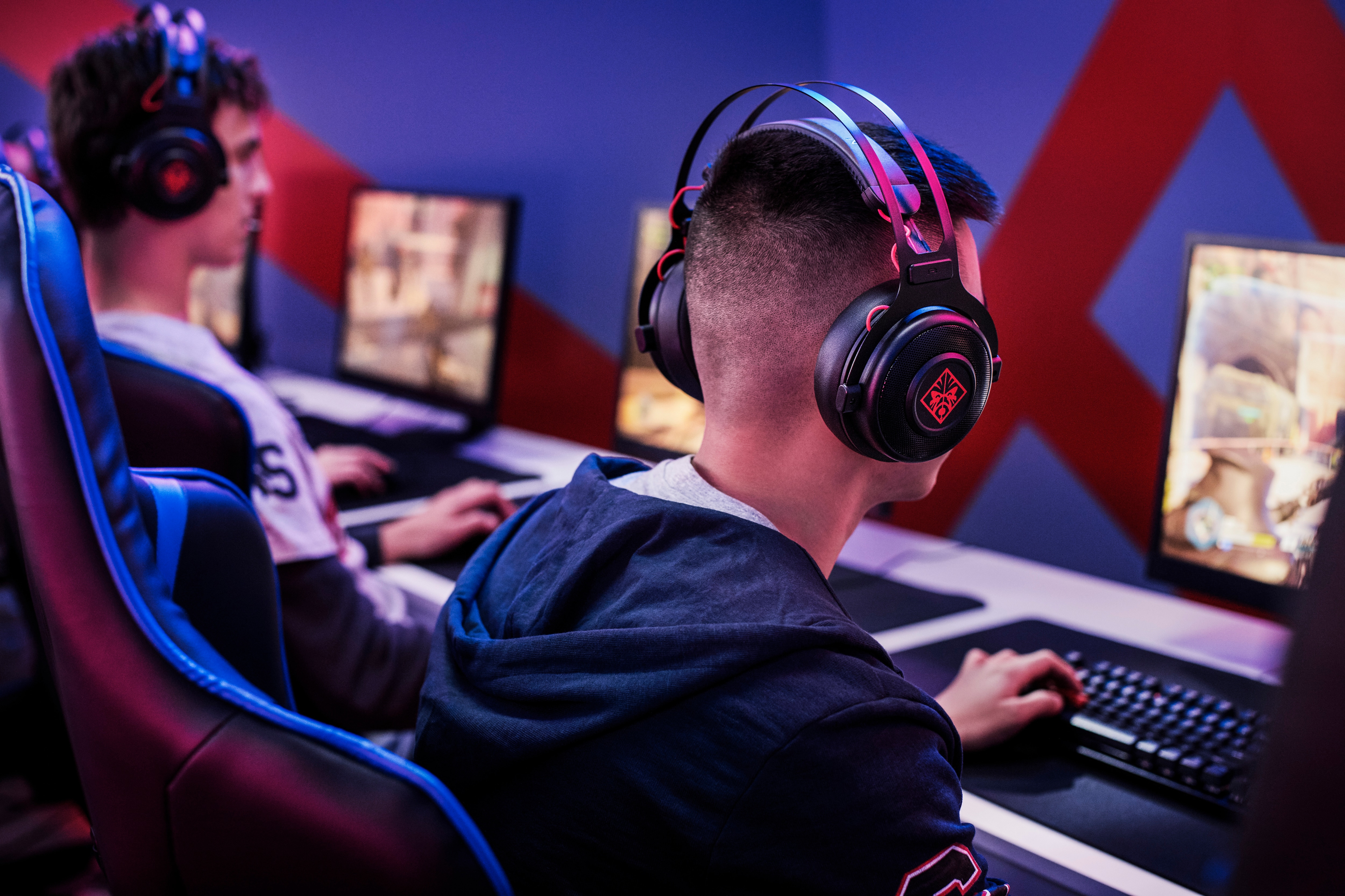 Zwei Spieler mit Kopfhörern spielen Spiele auf Computern mit rotem und blauem Hintergrund.