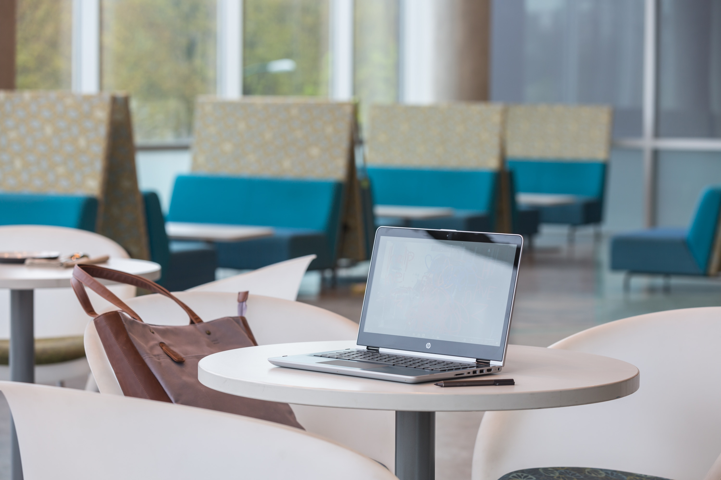 Ein Laptop und eine Tasche liegen auf einem runden Tisch in einer hellen Lounge.