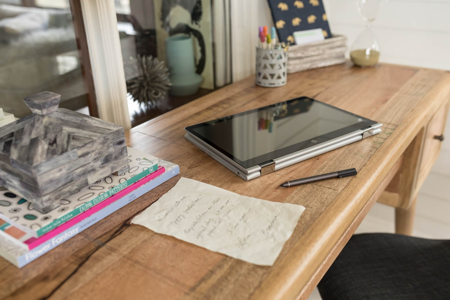 Ein Holztisch mit Laptop, Stift, handschriftlicher Notiz und gestapelten Büchern mit dekorativer Schachtel.