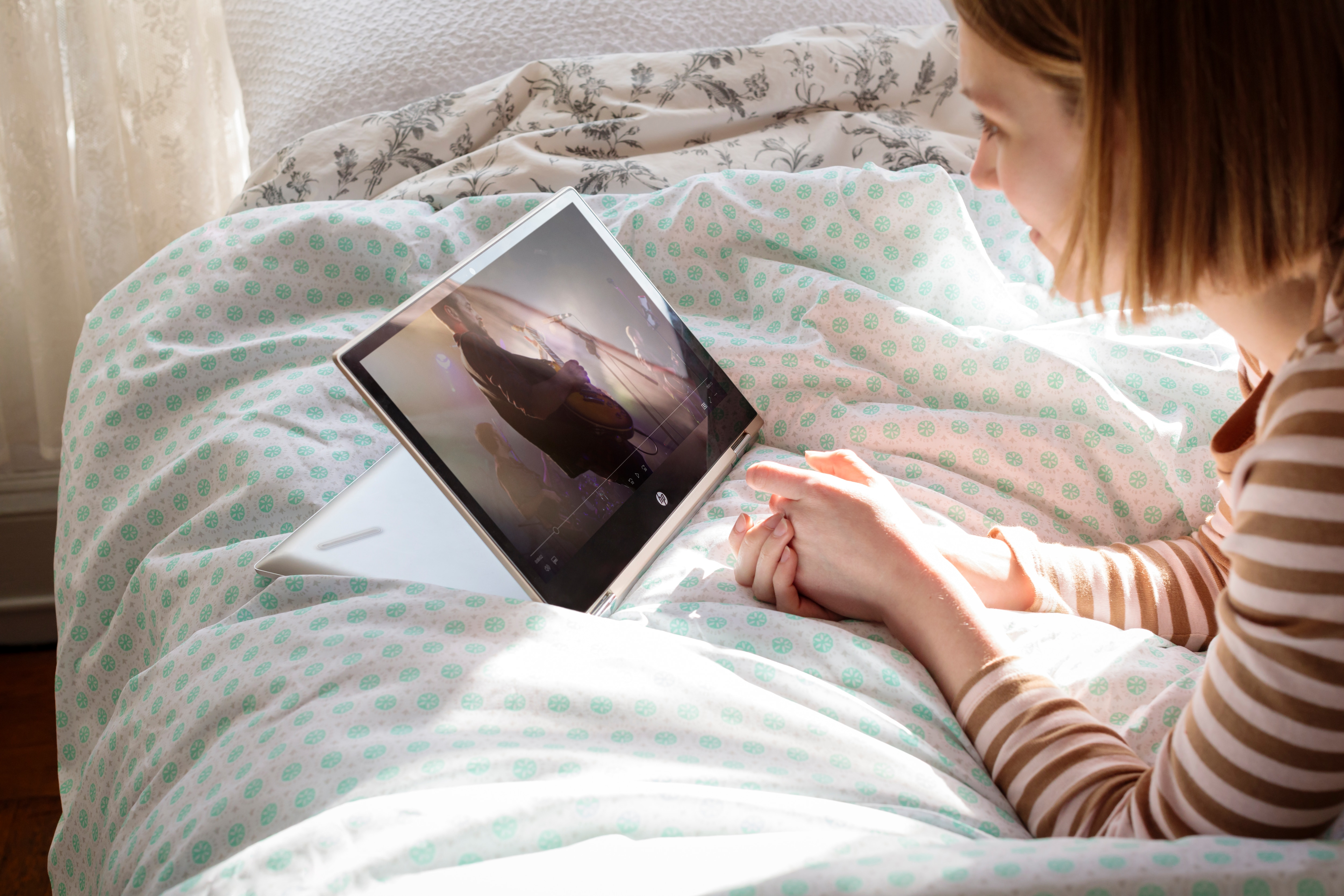 Eine Frau liegt im Bett und schaut sich ein Video auf einem Laptop an.