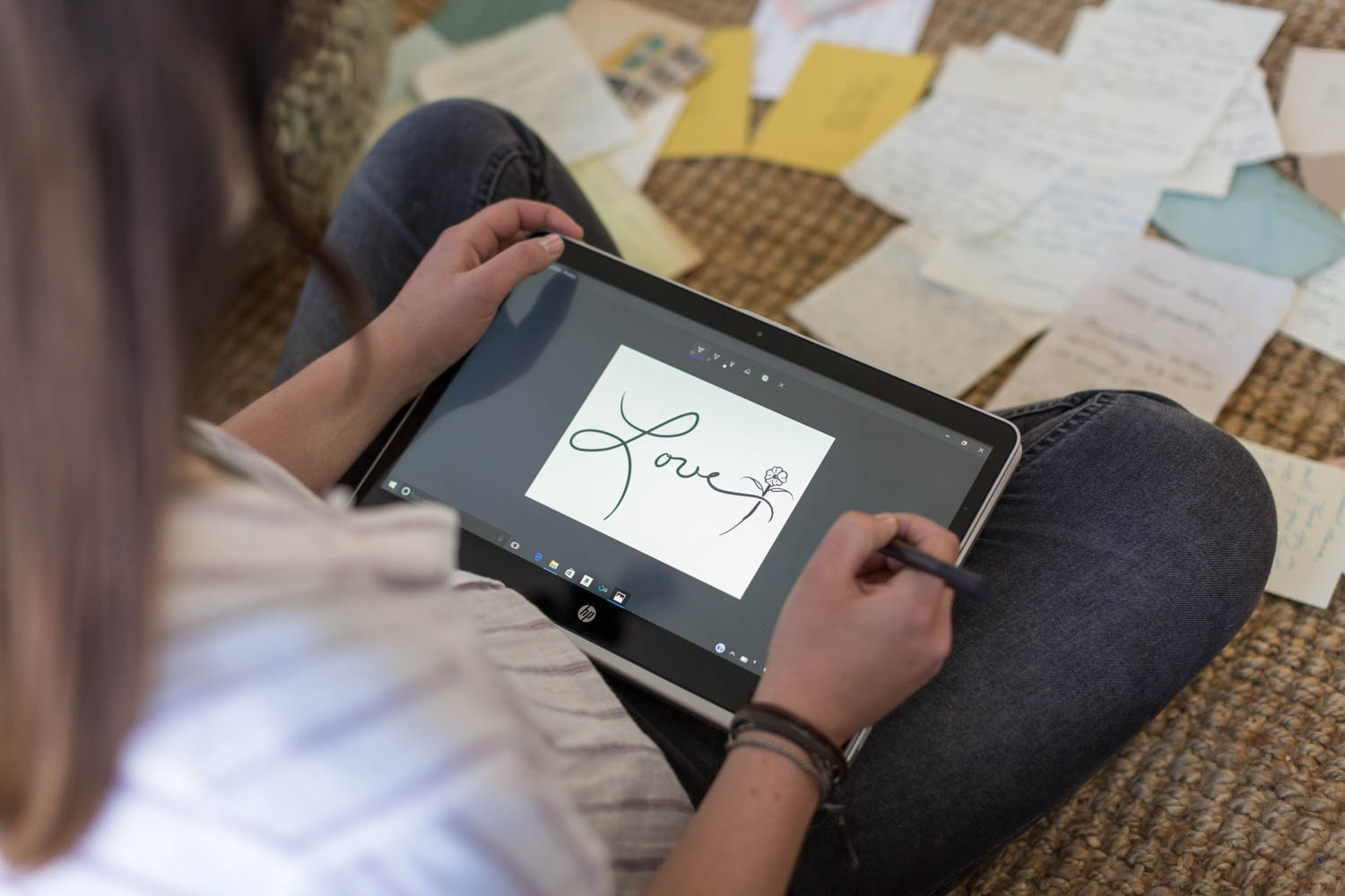Eine Person hält ein Tablet und zeichnet mit einem Eingabestift das Wort Liebe, umgeben von Notizen.