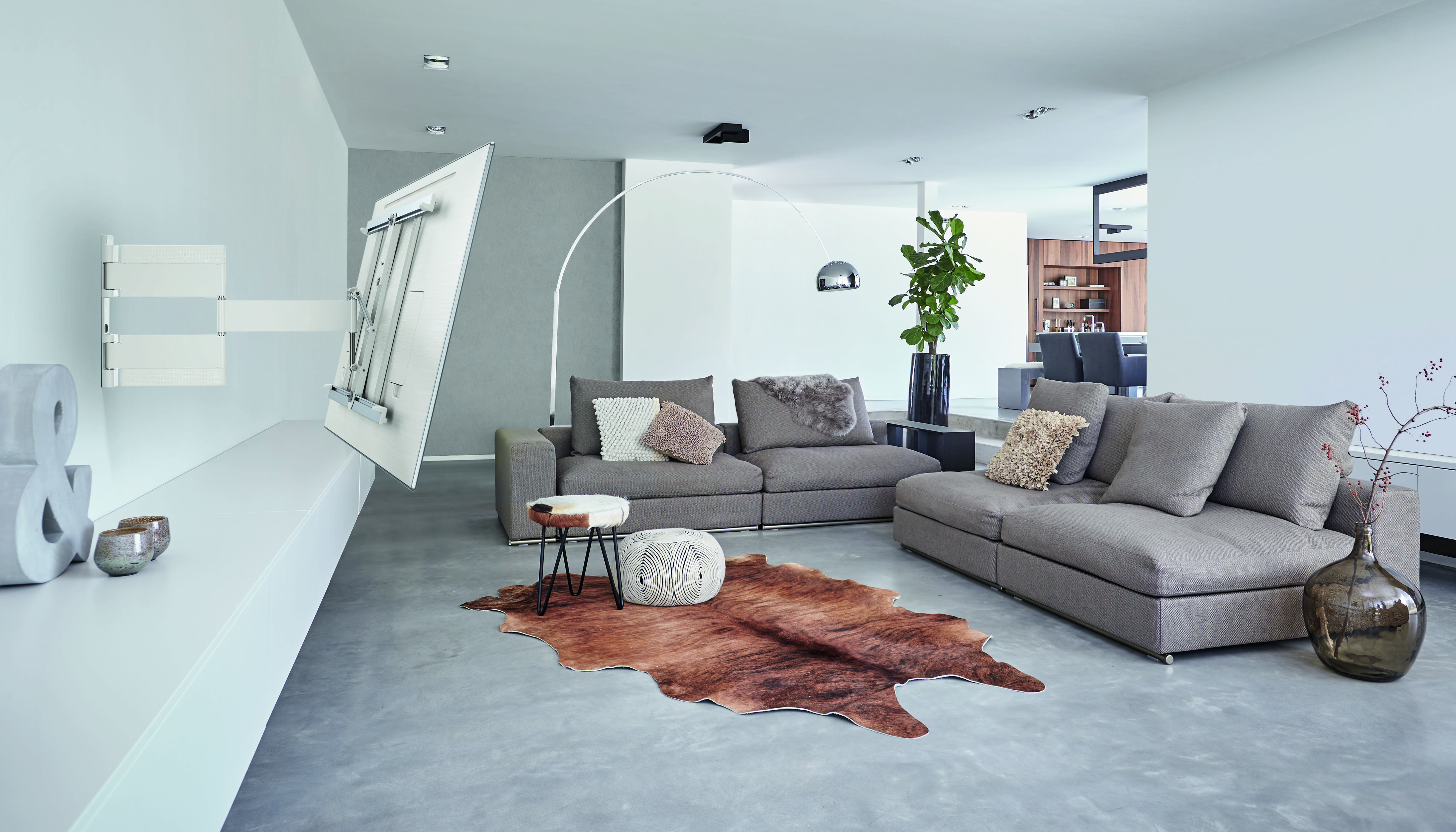 Modernes Wohnzimmer. Graues Sofa, brauner Teppich, weiße Wand. TV-Halterung an der Wand. Stehlampe.