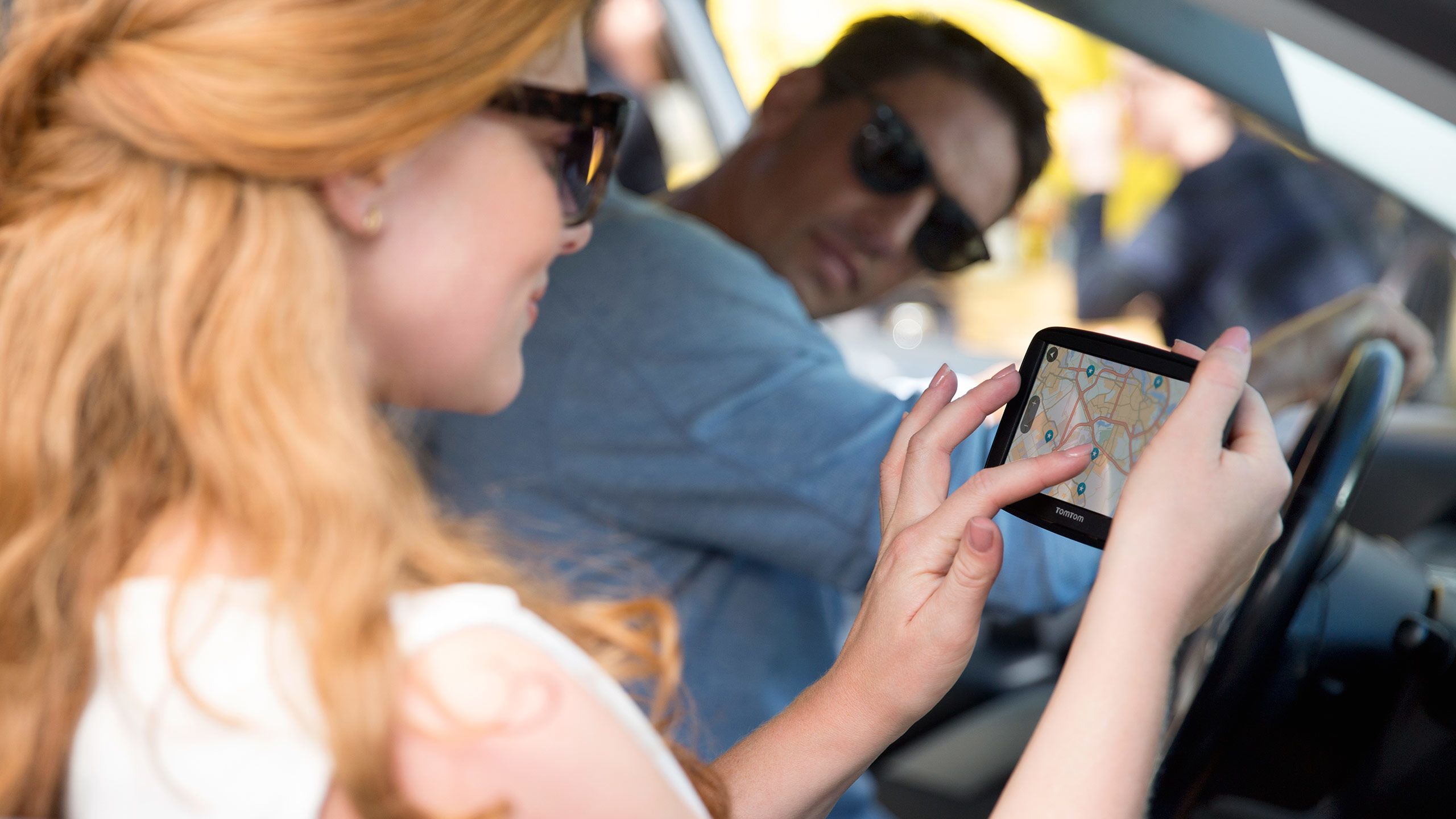 Eine Frau schaut auf eine Navigations-App auf ihrem Handy, während ein Mann das Auto fährt.