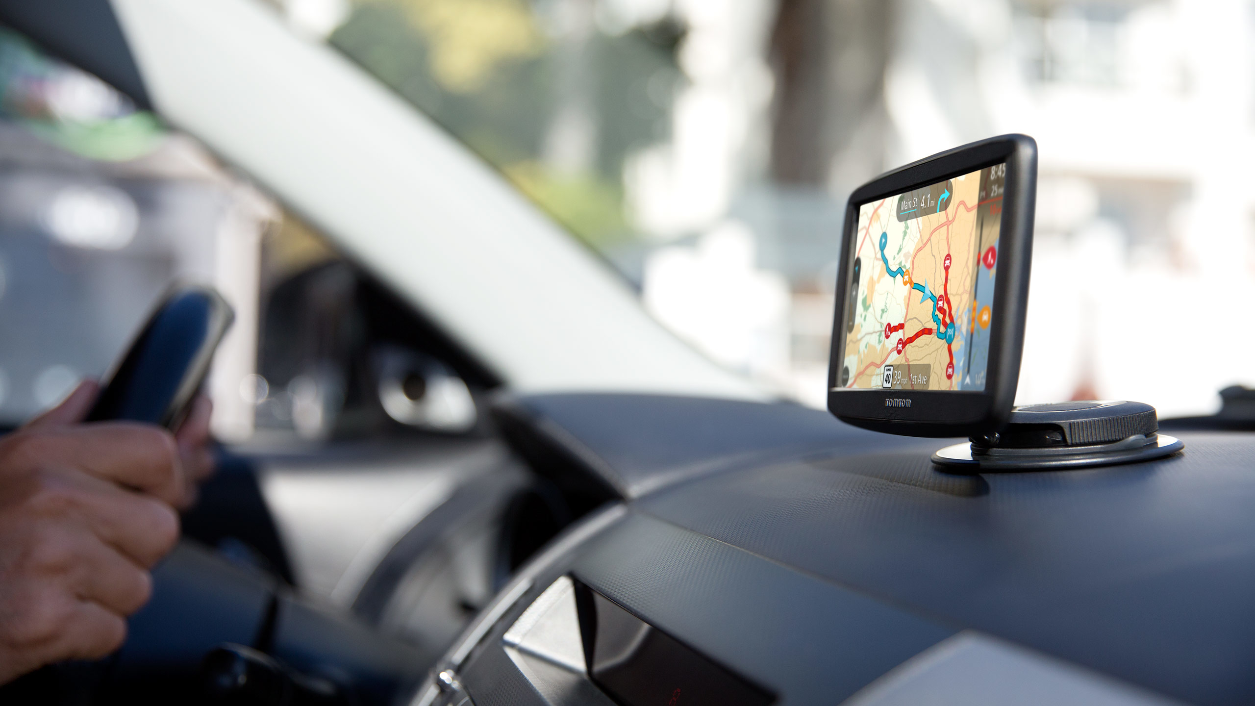 Ein GPS-Gerät auf dem Armaturenbrett zeigt eine Karte, eine Hand hält ein Telefon.