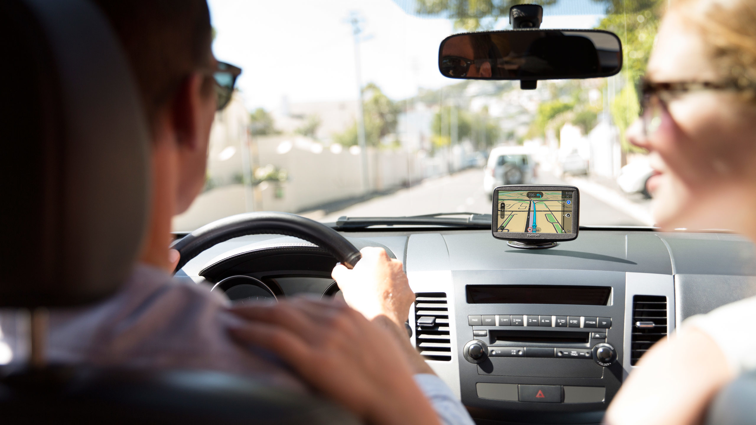 Paar im Auto mit GPS. Fahrer hält das Lenkrad. GPS zeigt Karte. Heller Tag.