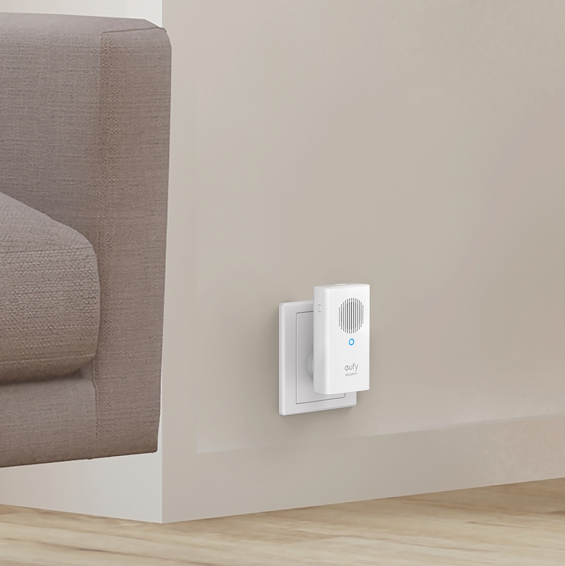 A white Eufy security device plugged into a wall socket next to a sofa.
