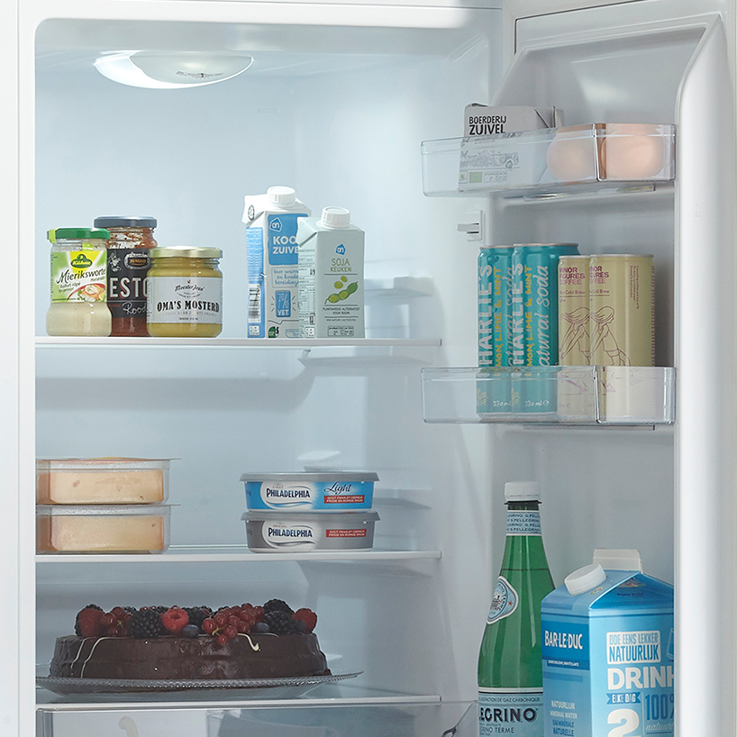 Refrigerator interior with food items on shelves, including jars, drinks, and a cake.