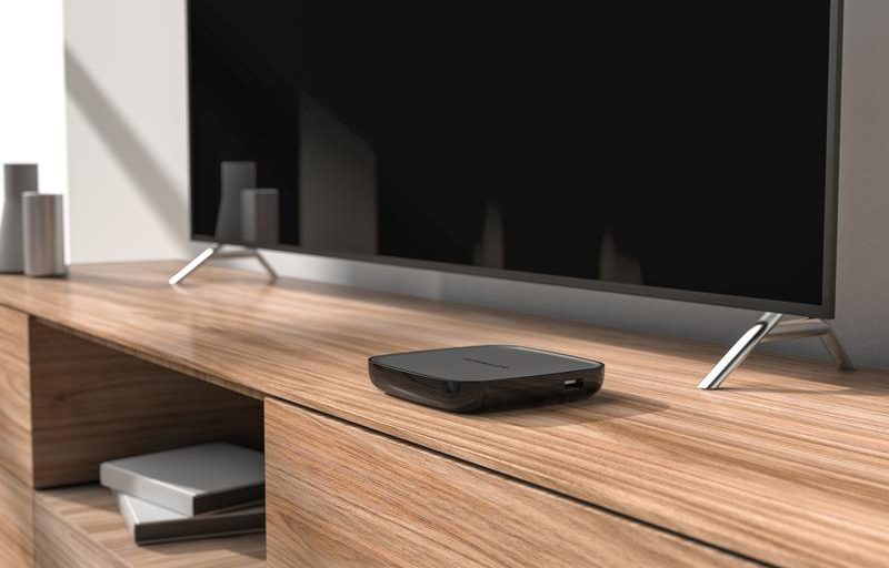 Un lettore multimediale nero è su un ripiano in legno sotto una TV con gambe argentate.
