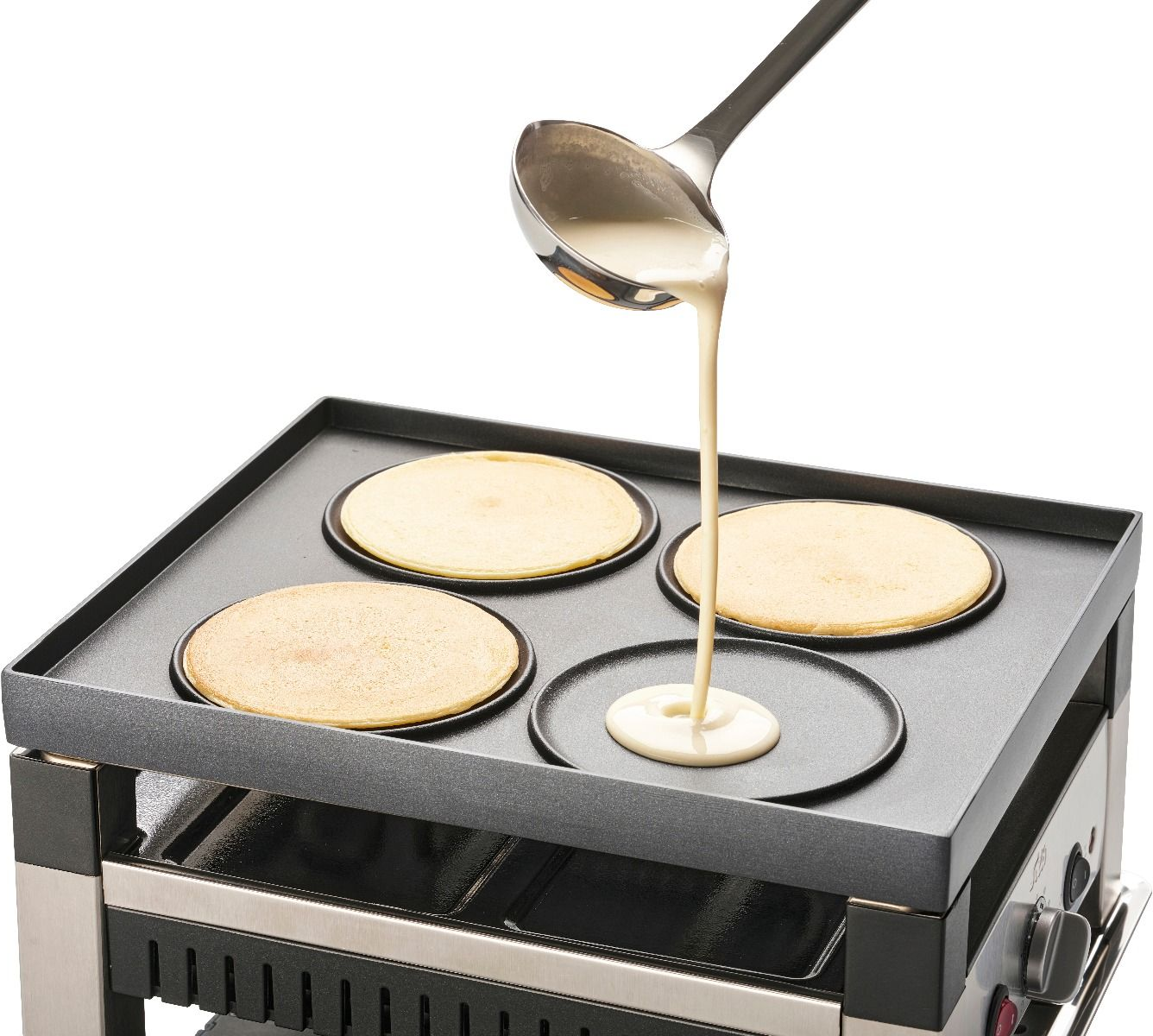 Pâte à crêpes versée sur une plaque chauffante avec quatre moules. Trois crêpes cuisent.