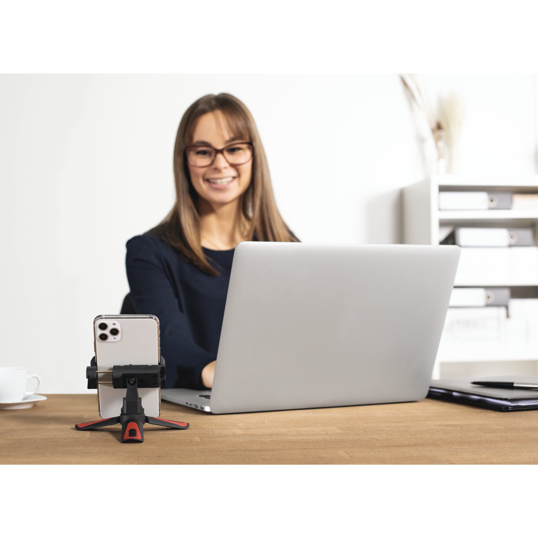 Frau benutzt Laptop mit Telefon auf Stativ montiert.