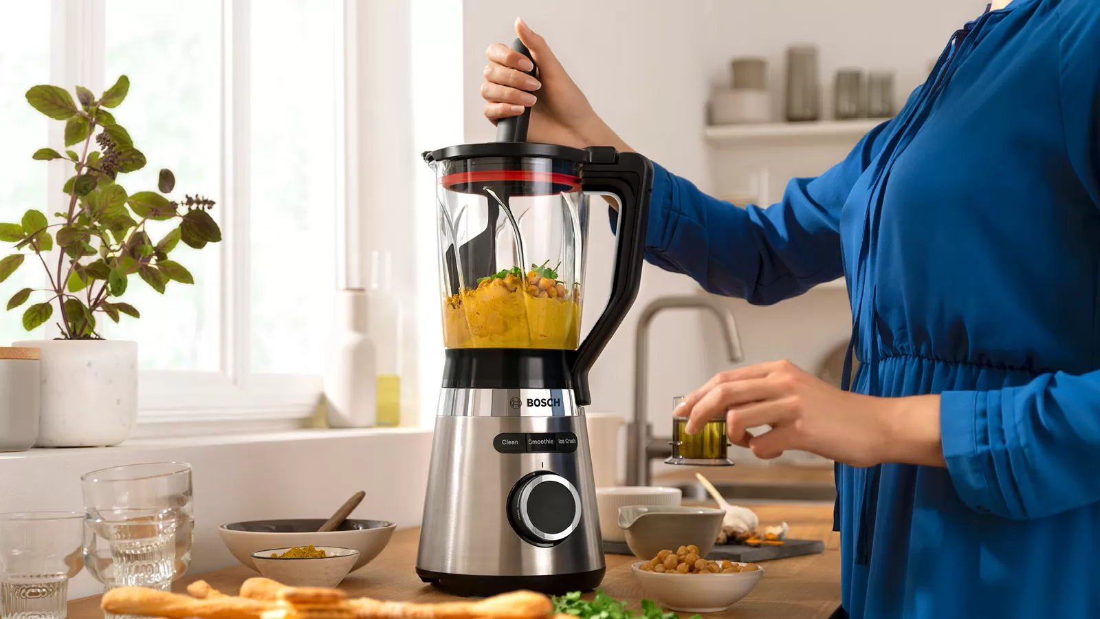 Een vrouw voegt vloeistof toe aan een blender. De blender heeft kikkererwten.