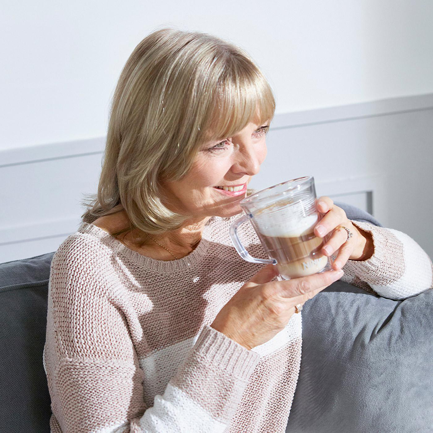 Eine Frau, die ein Kaffeegetränk hält und lächelt.