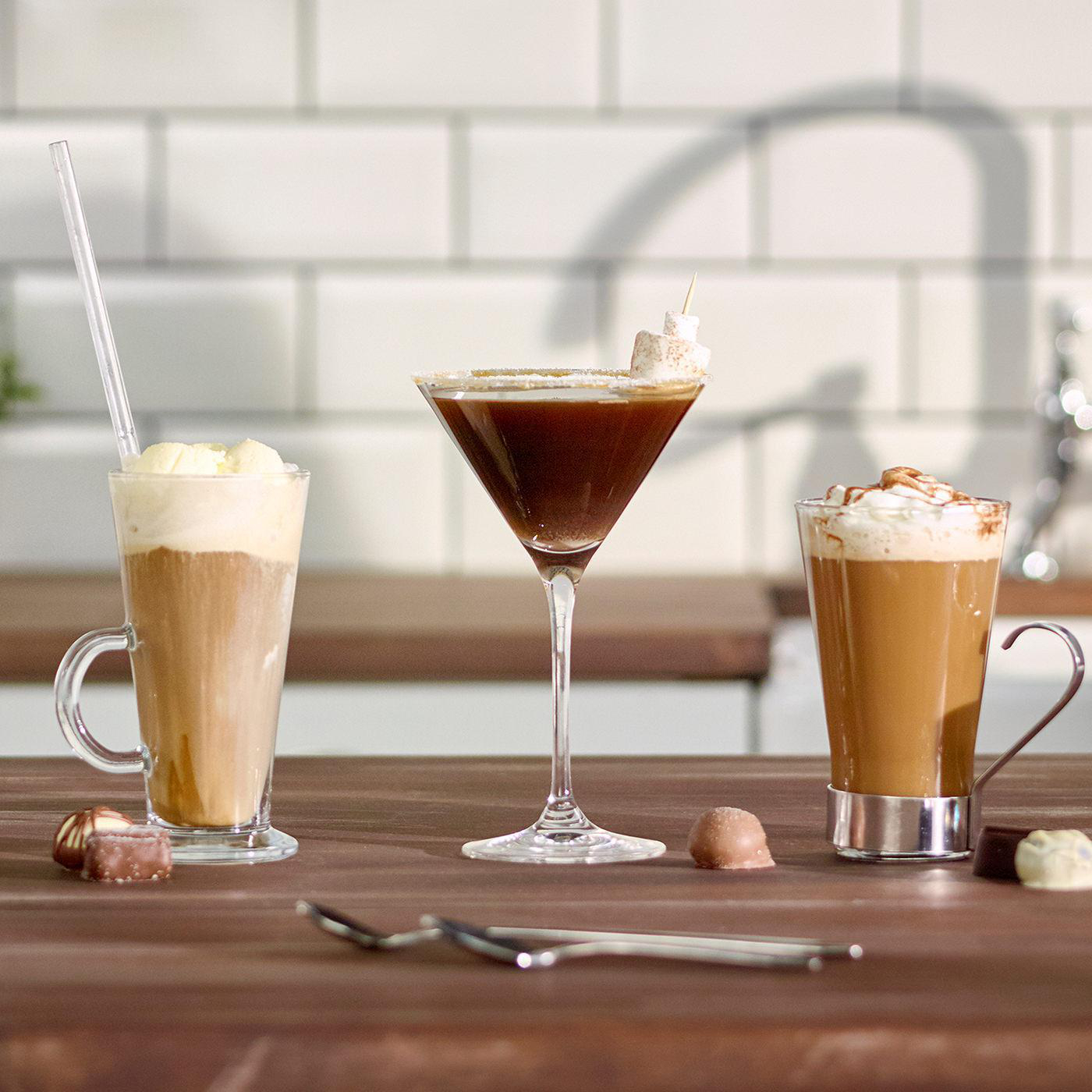Drei Cocktails auf einem Holztisch mit Pralinen.