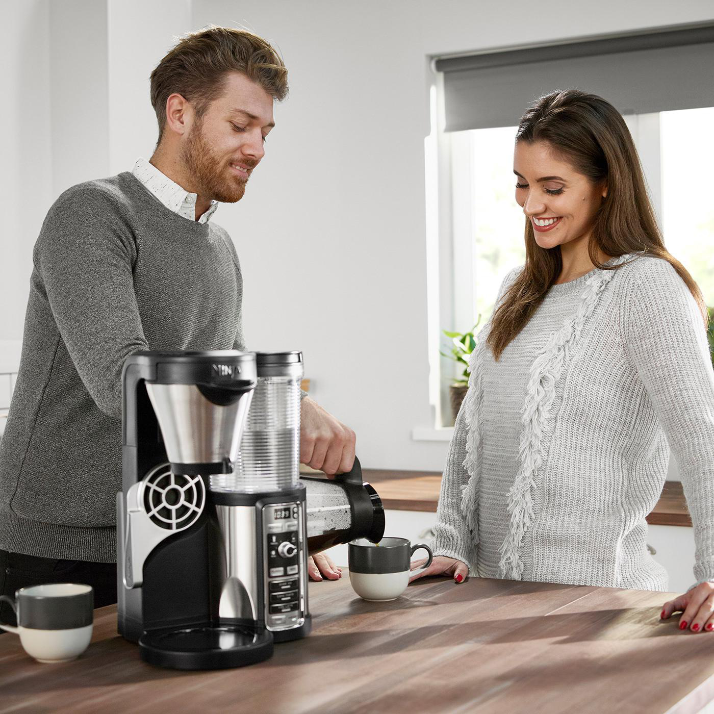 Paar gießt Kaffee ein, mit einer Ninja Kaffeemaschine, in einer Küche.