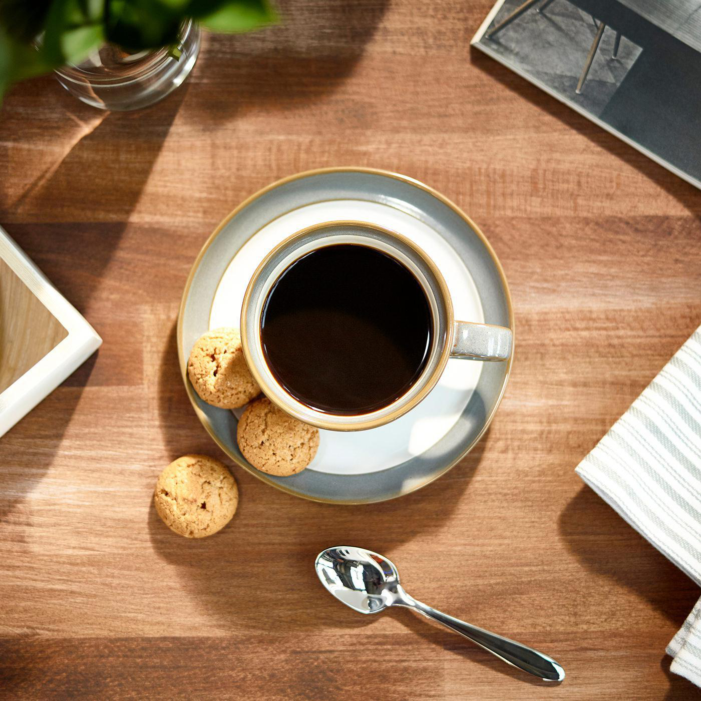 Draufsicht auf Kaffeetasse, Untertasse, Kekse und Löffel auf einem Holztisch.