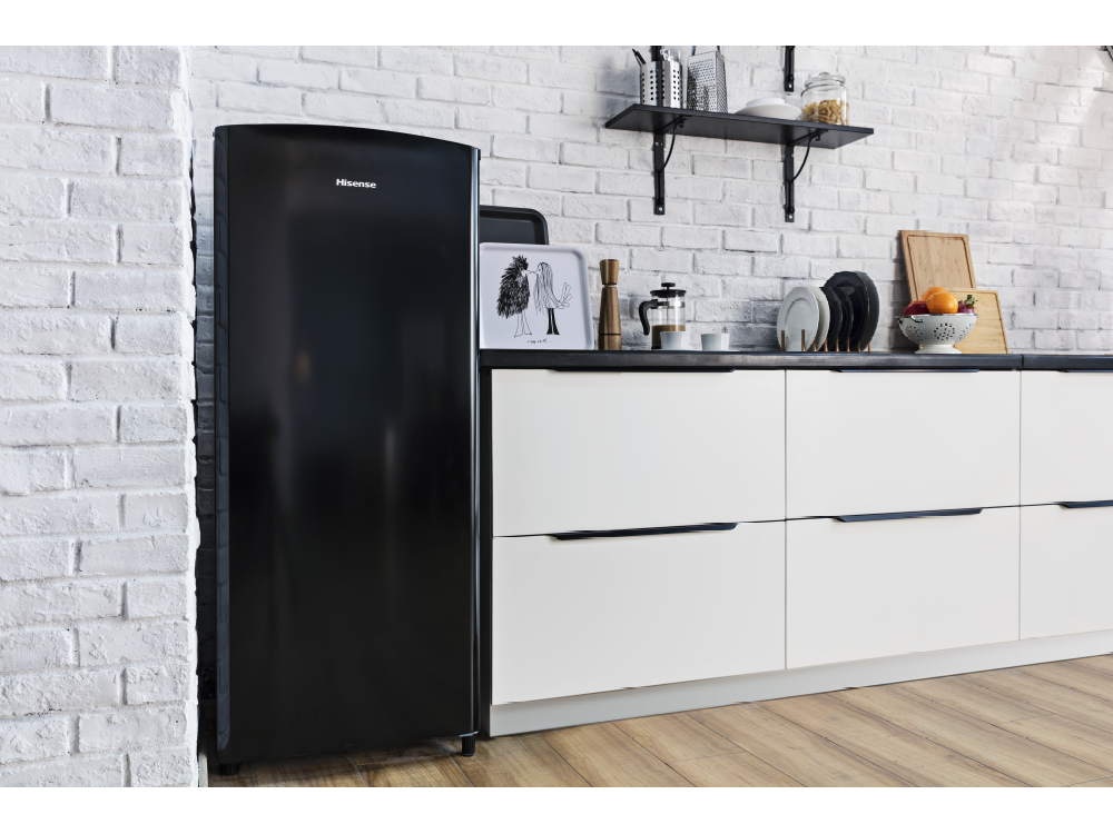 Refrigerador negro contra pared de ladrillo blanco, con gabinetes blancos.