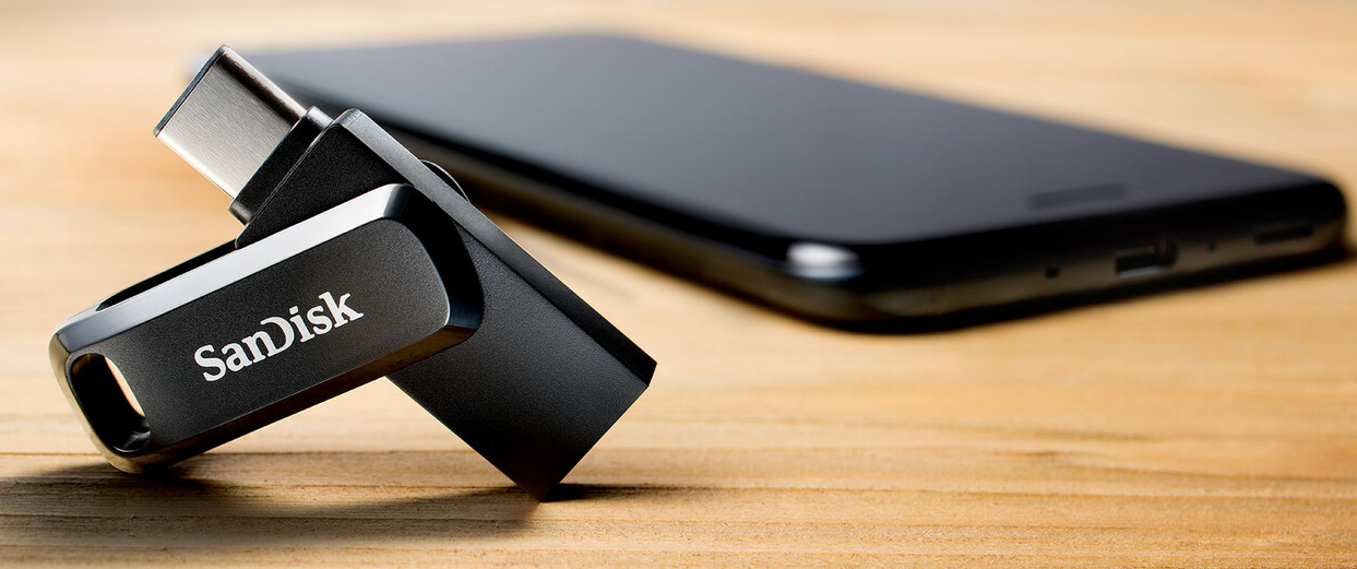 Clé USB Sandisk avec un téléphone sur une surface en bois.