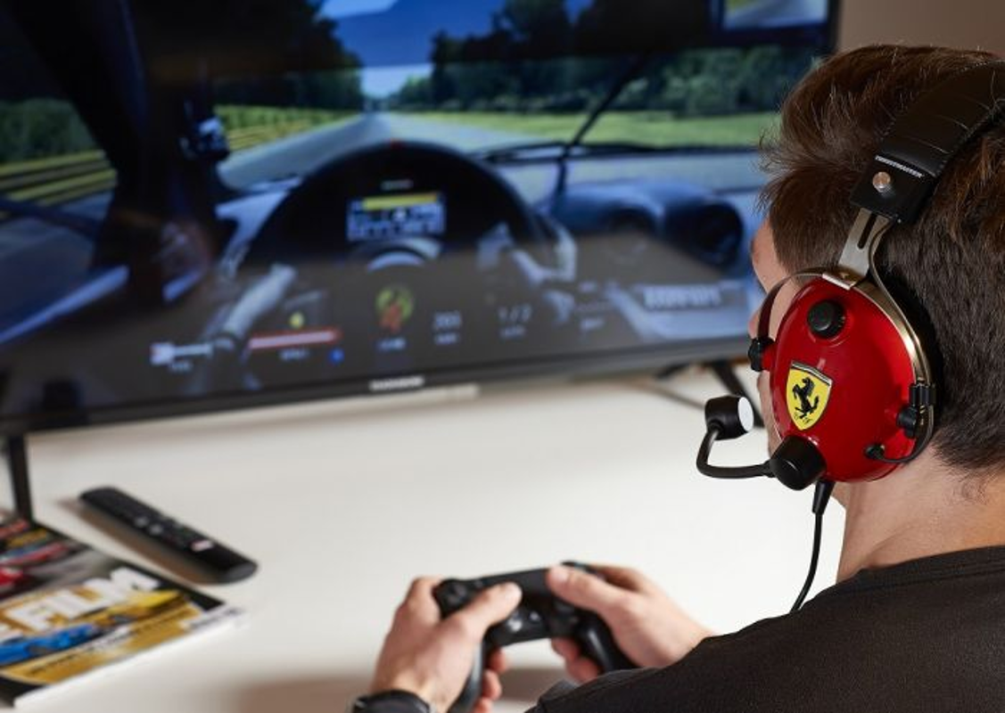 Homme portant un casque Ferrari rouge jouant à un jeu de course sur une télévision avec une manette.