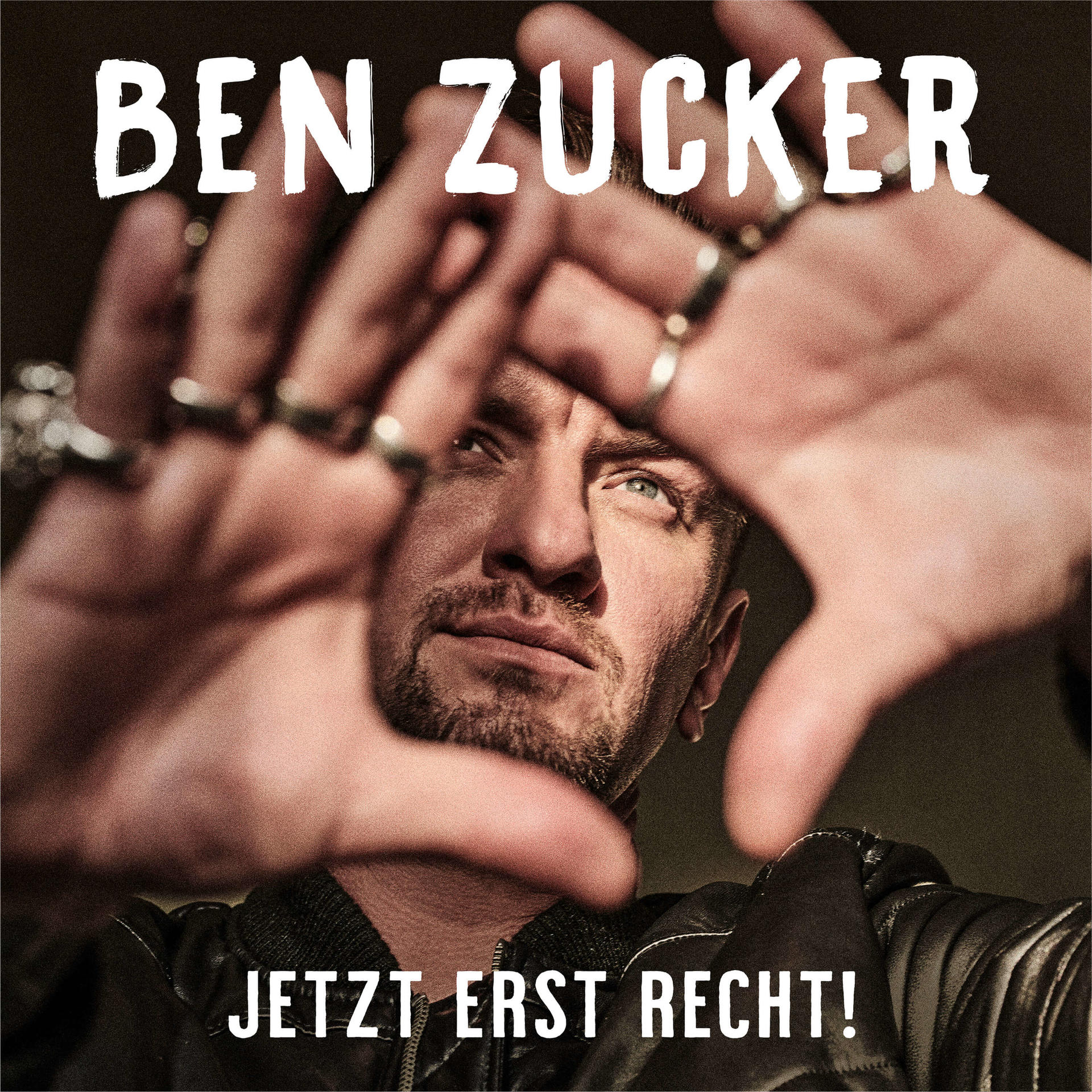 Mann, der von Händen vor seinem Gesicht eingerahmt wird, mit Text oben und unten.