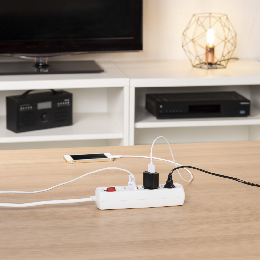 Ein Mehrfachstecker mit einem Smartphone, Ladegerät und einem Stecker auf einem Holztisch.