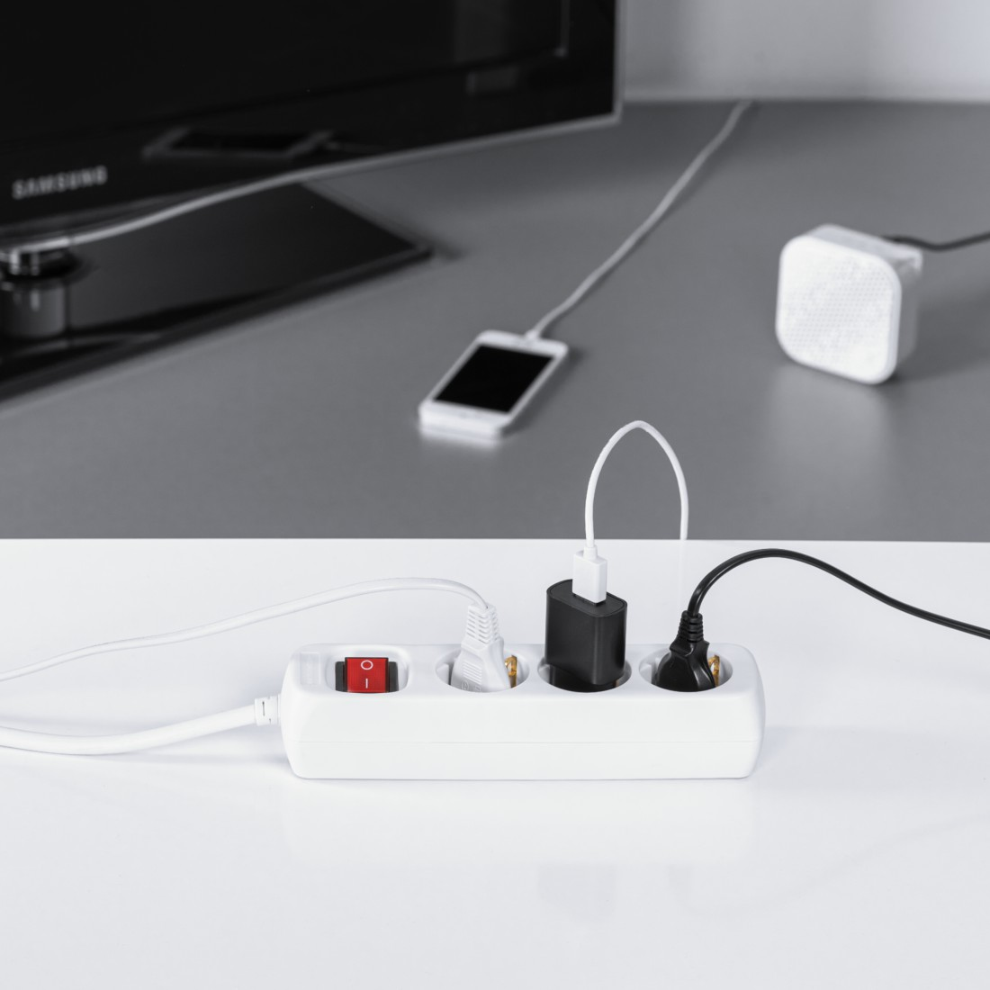 Eine weiße Steckdosenleiste mit drei Steckplätzen, einem roten Schalter, zwei Adaptern und einem Stecker.