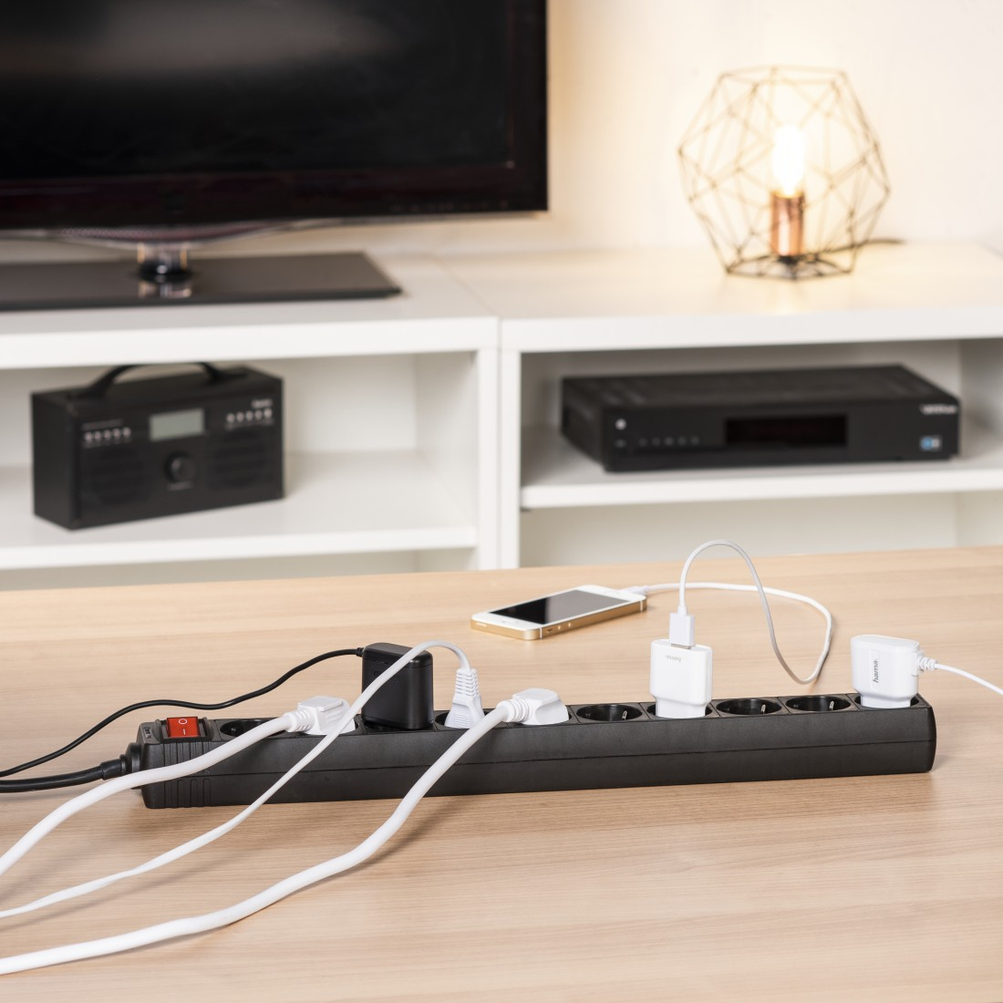 Steckdosenleiste mit mehreren Steckern und Geräten. Lampe, Telefon und schwarze Box enthalten.