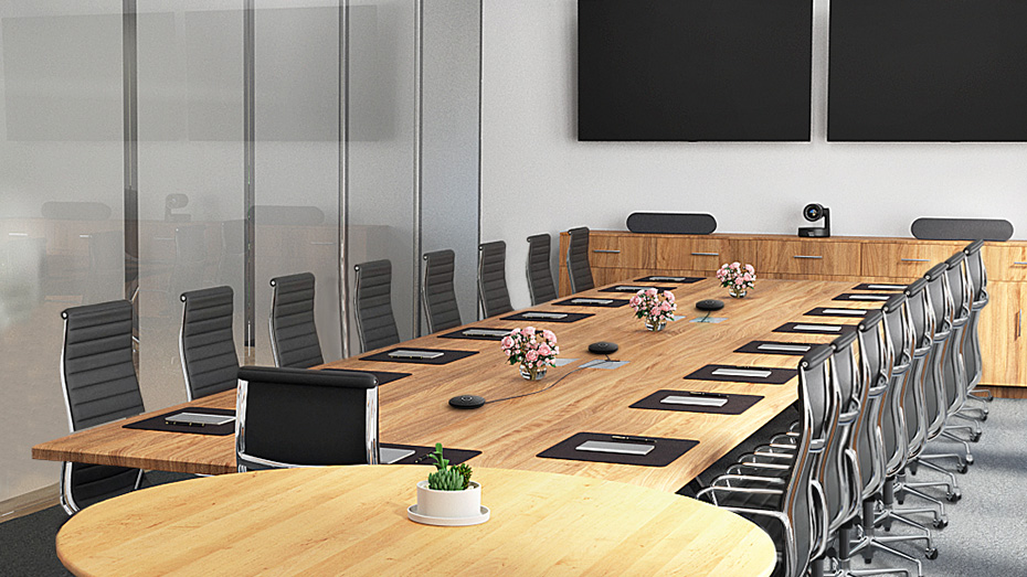 Konferenzraum mit langem Holztisch, Stühlen und zwei Bildschirmen an der Wand. Eine kleine Pflanze.