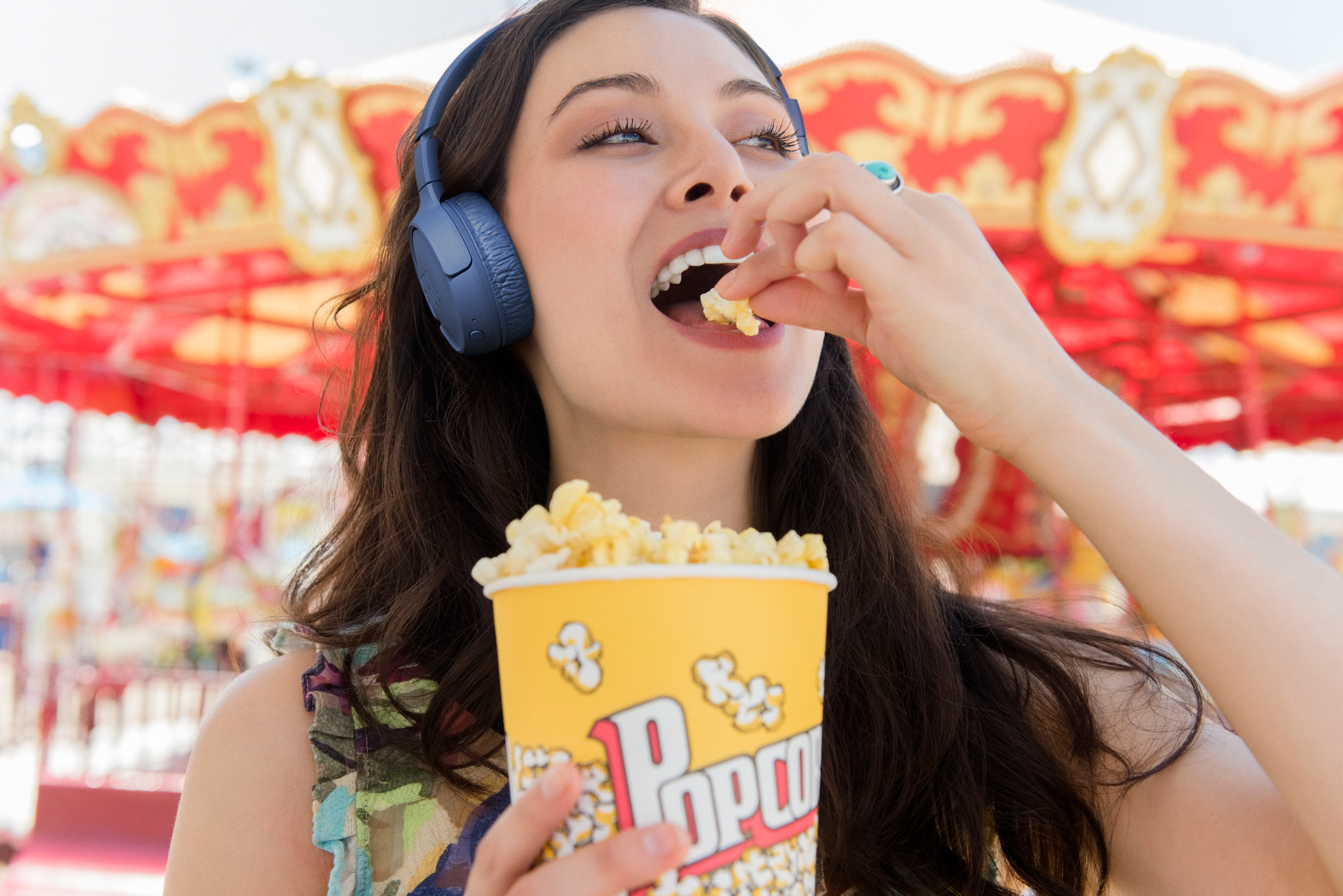 Une femme mangeant du pop-corn, portant un casque, avec un manège en arrière-plan.