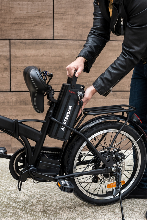 Persona colocando una batería en una bicicleta eléctrica negra, en un patio.