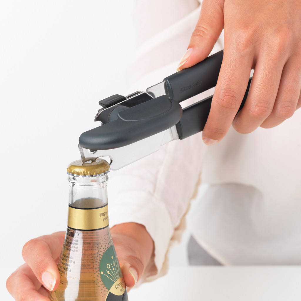 A person opening a ginger ale bottle with a bottle opener. The bottle opener is dark gray.