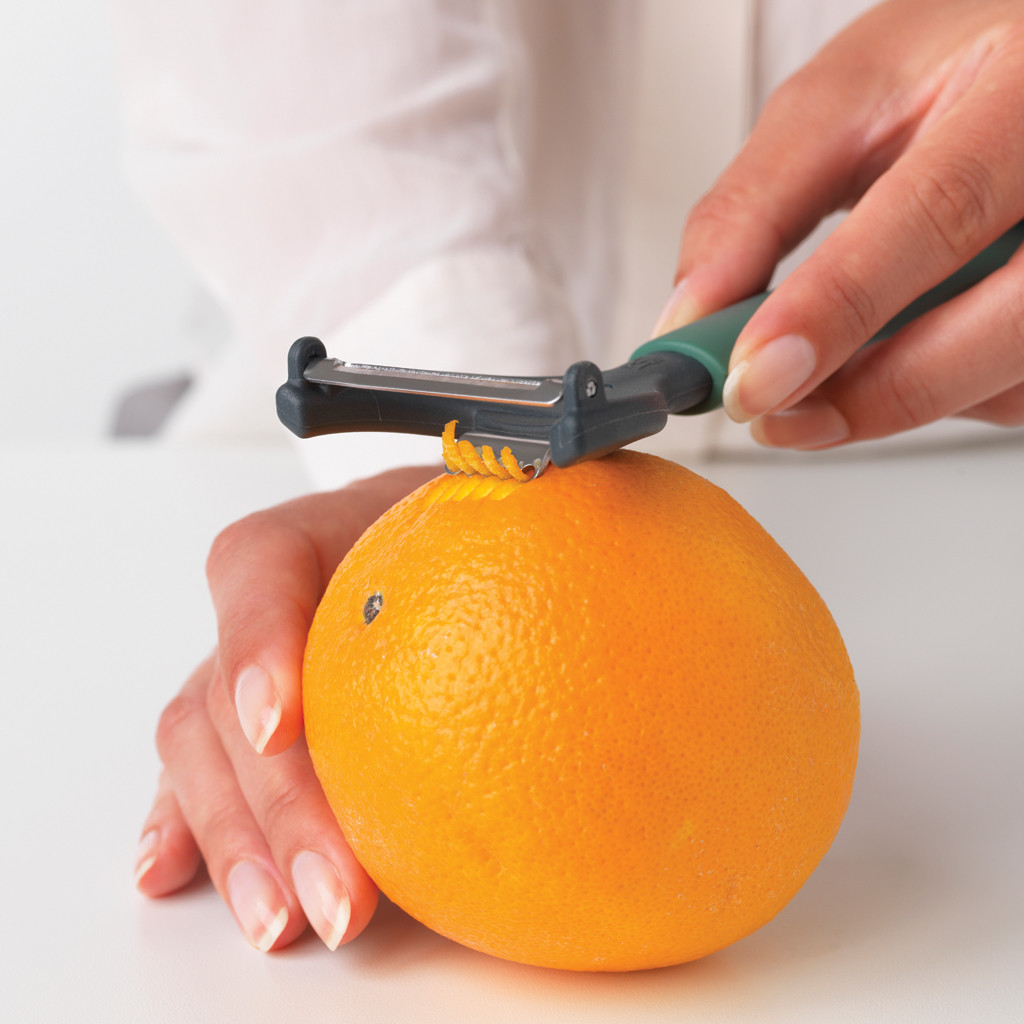 A person peeling an orange with a peeler. The orange is bright orange. The background is white.