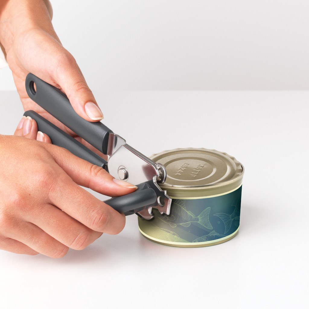Hands using a can opener to open a can of food. The can has a fish design. White surface.