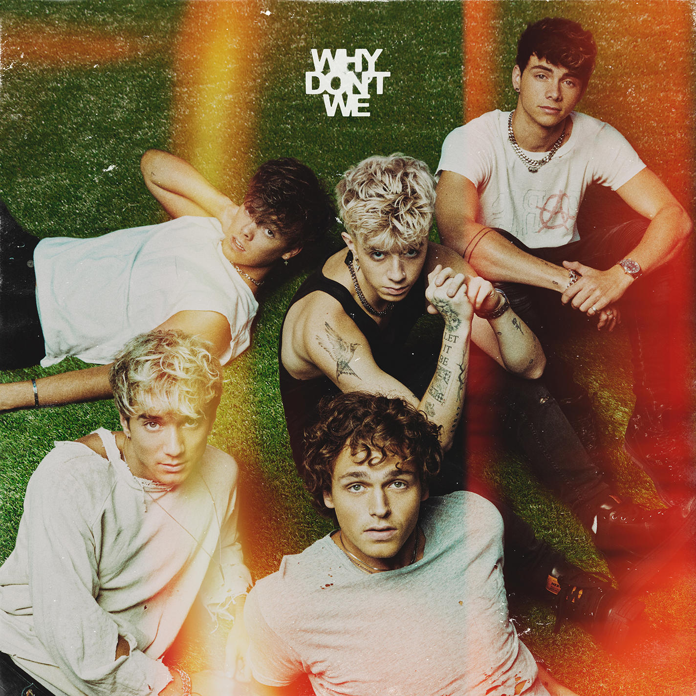 Bandfoto: 5 Männer auf Gras. Text: 'WHY DON'T WE'. Gefiltert mit orangem Licht.