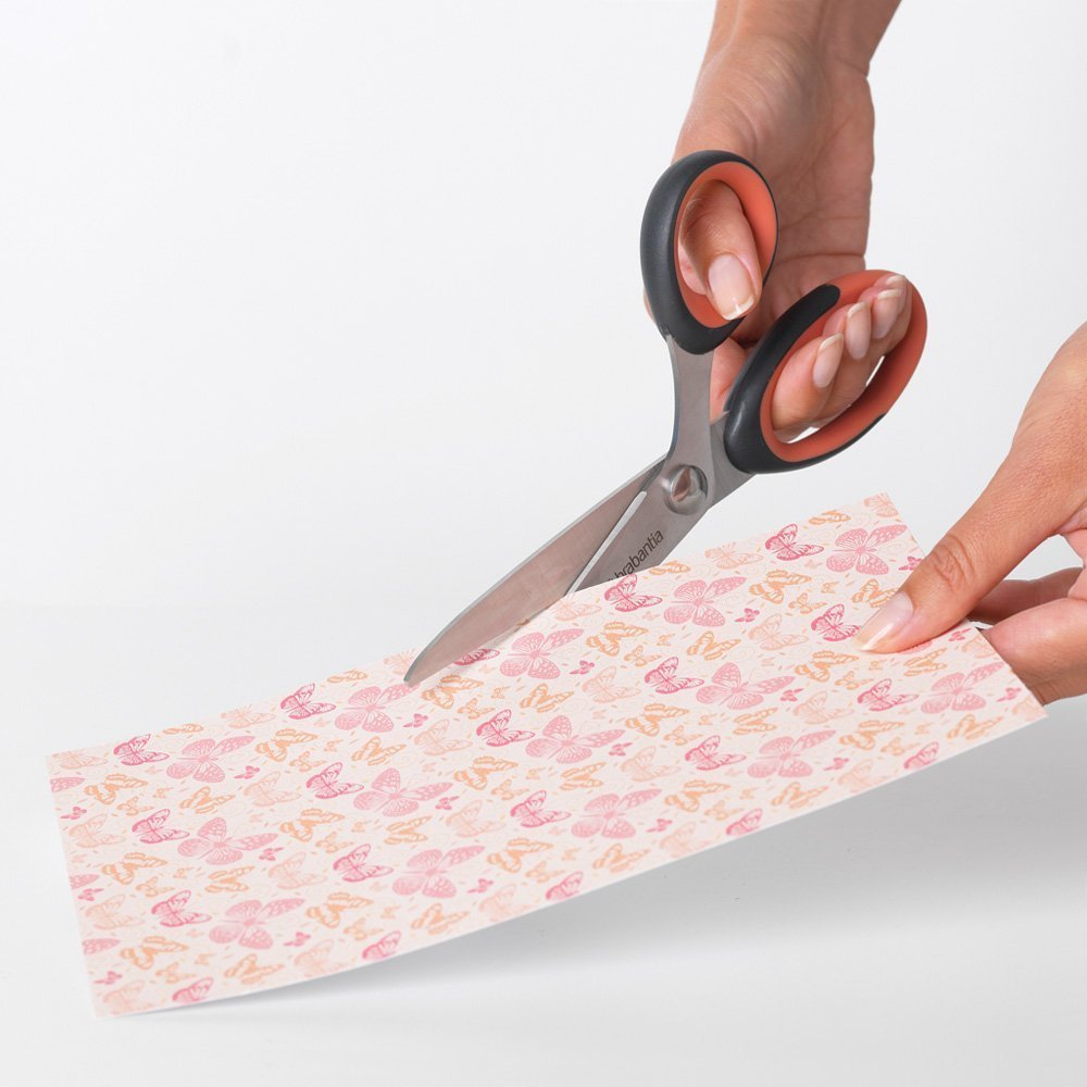 Hands are cutting a paper with butterfly pattern using scissors. The scissors are silver and black with orange handles.