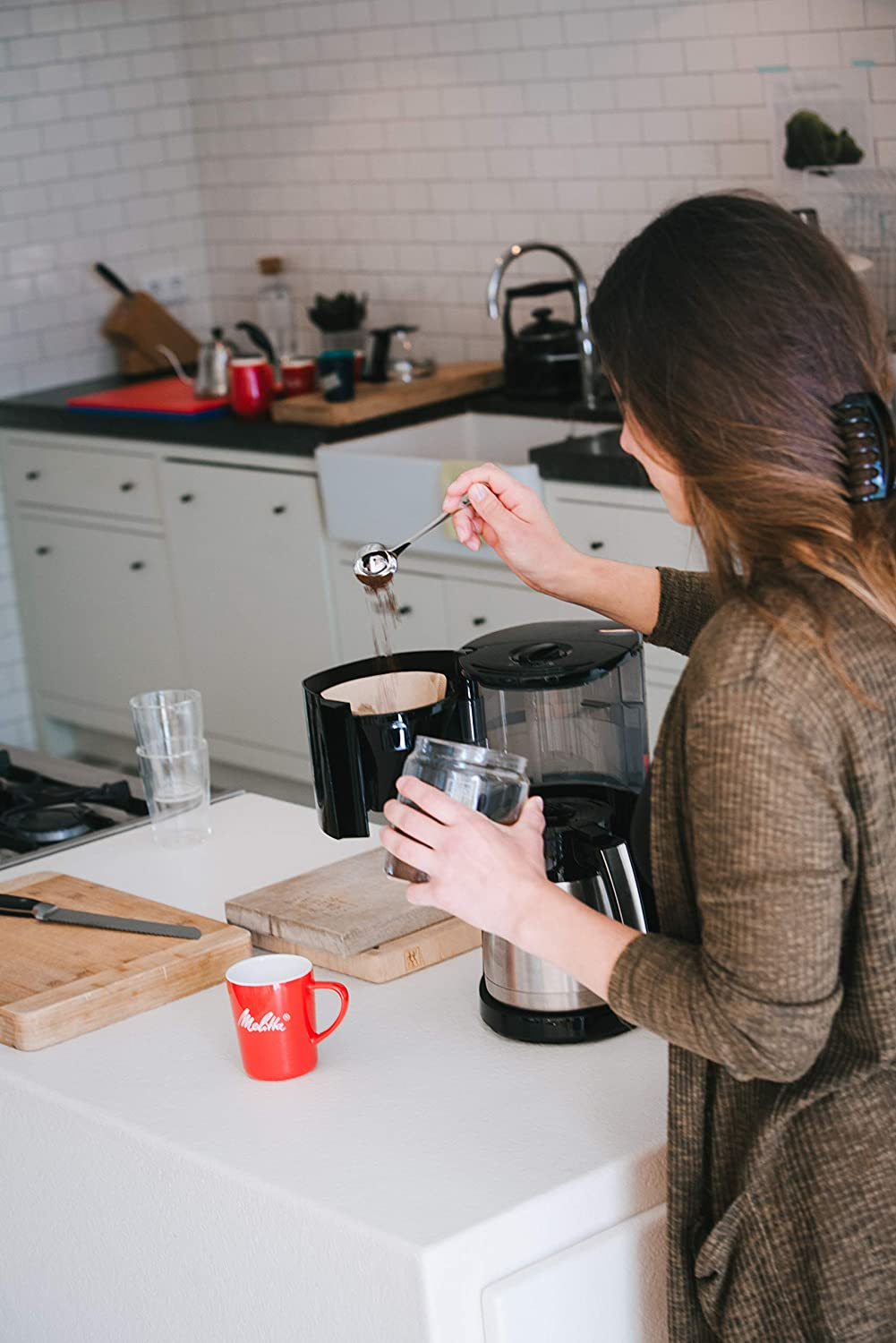 Woman adding coffee grounds to a filter, mug, and a wooden cutting board.