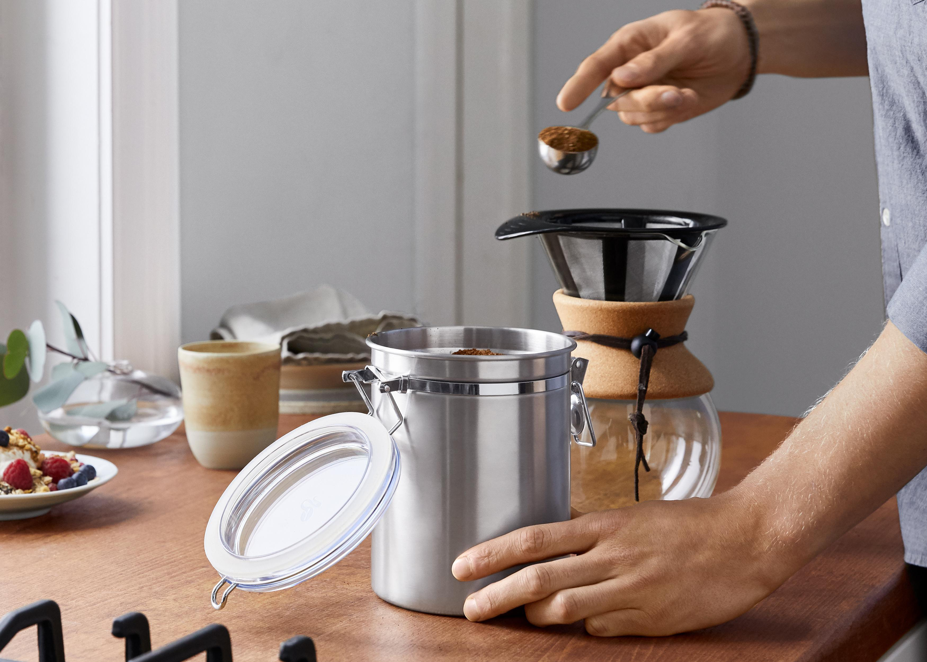 Person fügt Kaffeepulver in einen Edelstahlbehälter hinzu.