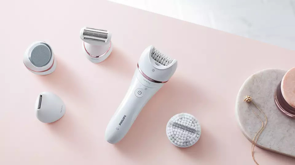 A set of white Philips epilation devices on a pink surface with accessories.