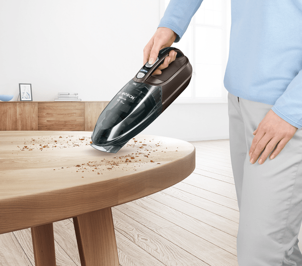 Eine Frau, die einen Holztisch mit einem Handstaubsauger absaugt.