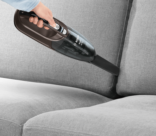 Eine Hand, die ein graues Sofa absaugt. Der Staubsauger ist schwarz und das Sofa grau.