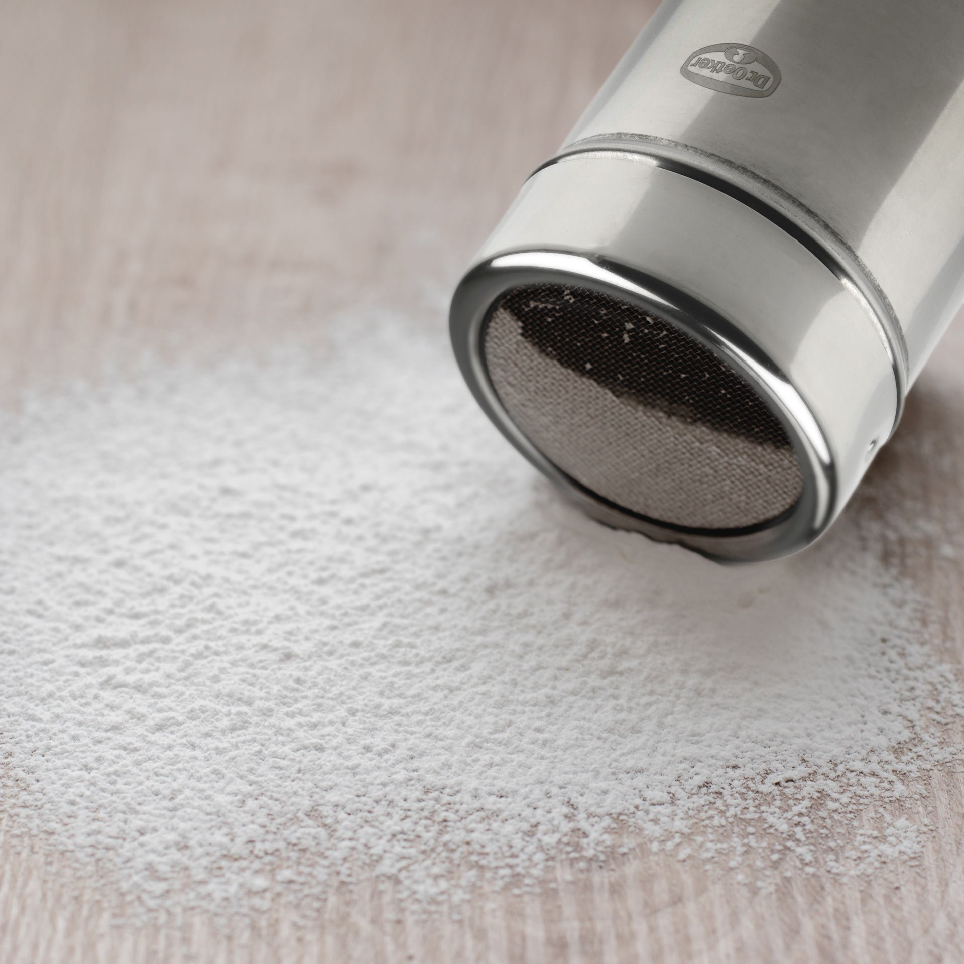Ein Edelstahl-Shaker mit Puderzucker auf einer Holzoberfläche.