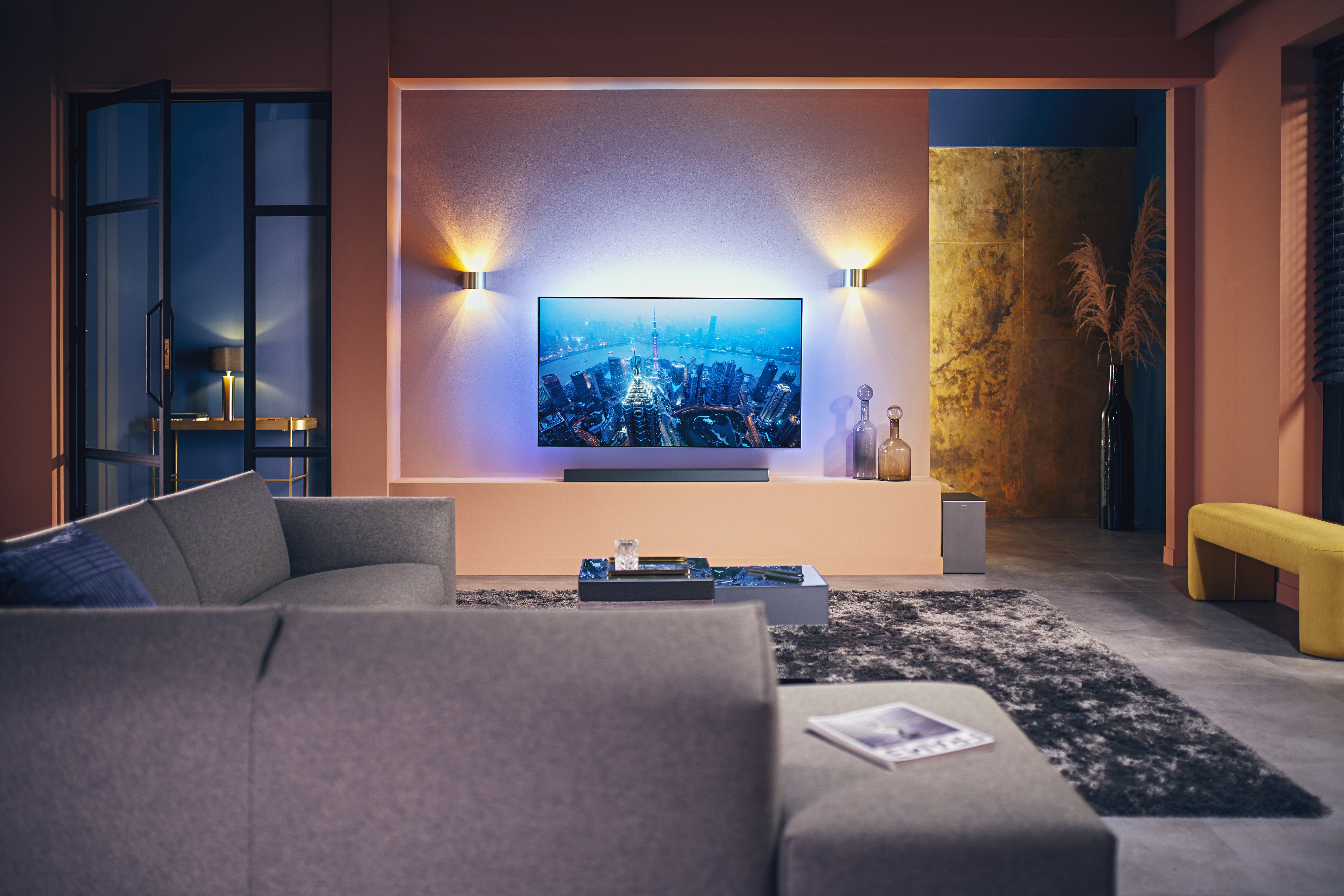 Wohnzimmer mit Fernseher, Couch und Teppich. Der Raum hat Umgebungslicht von Wandleuchten.